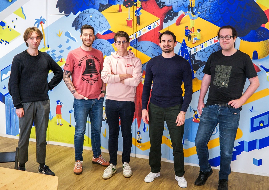 Cinq hommes debout devant un mur coloré avec un motif artistique vibrant.