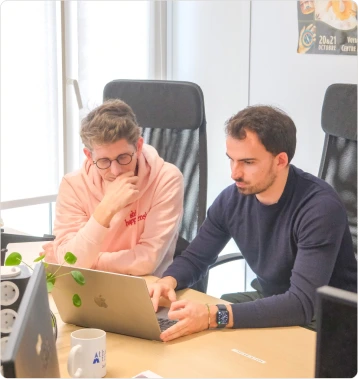 Deux hommes collaborant ensemble sur un ordinateur portable à une table de bureau moderne.