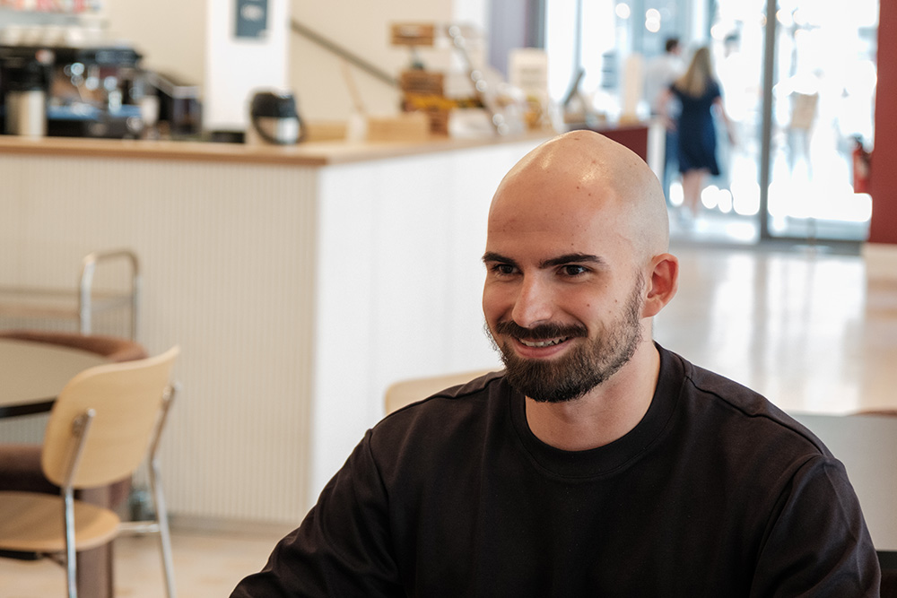 Trois hommes regardent des écrans d'ordinateur, l'un tenant une tasse, dans un bureau lumineux.