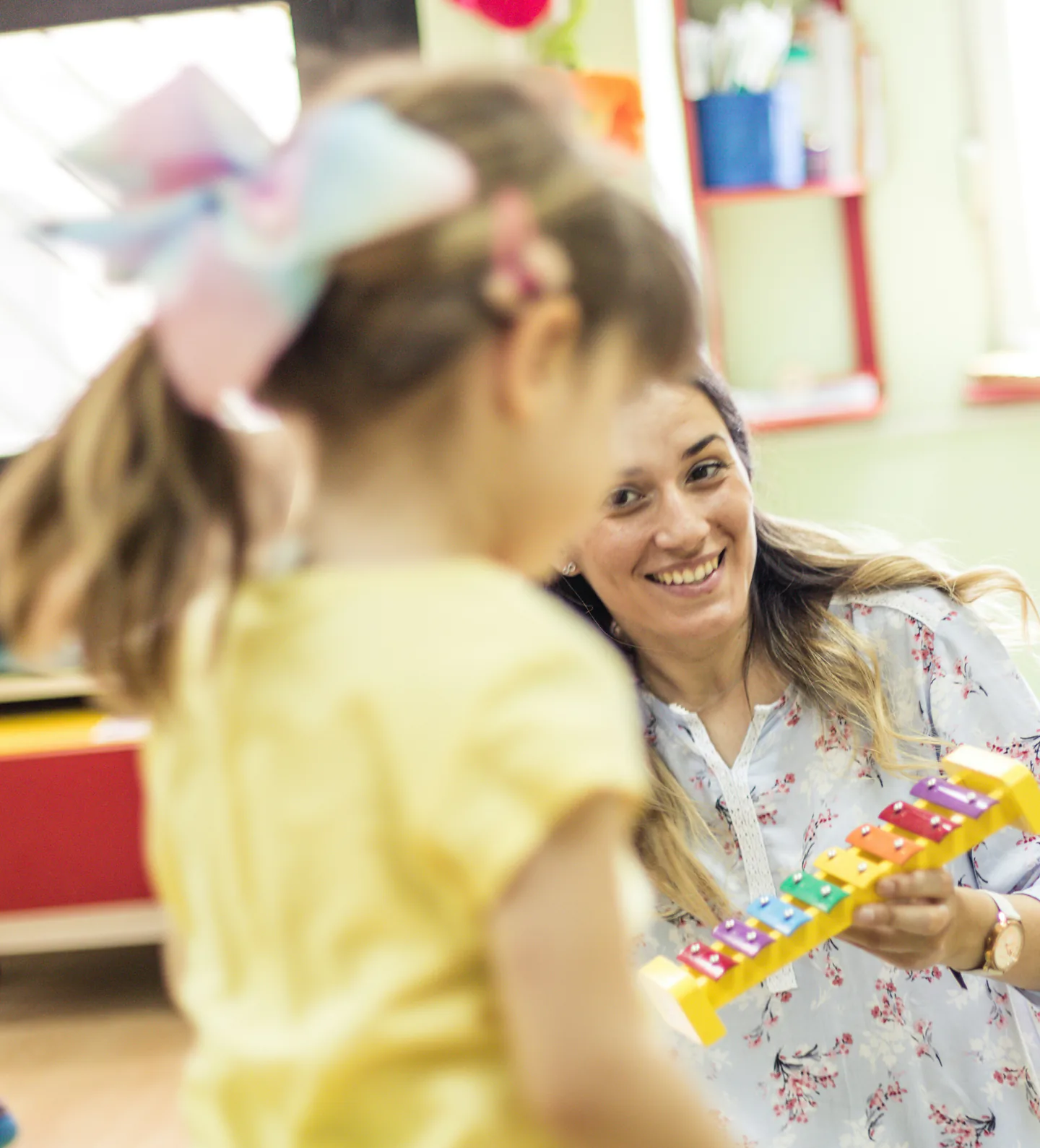 Une éducatrice joue du xylophone avec une petite fille dans une salle colorée.