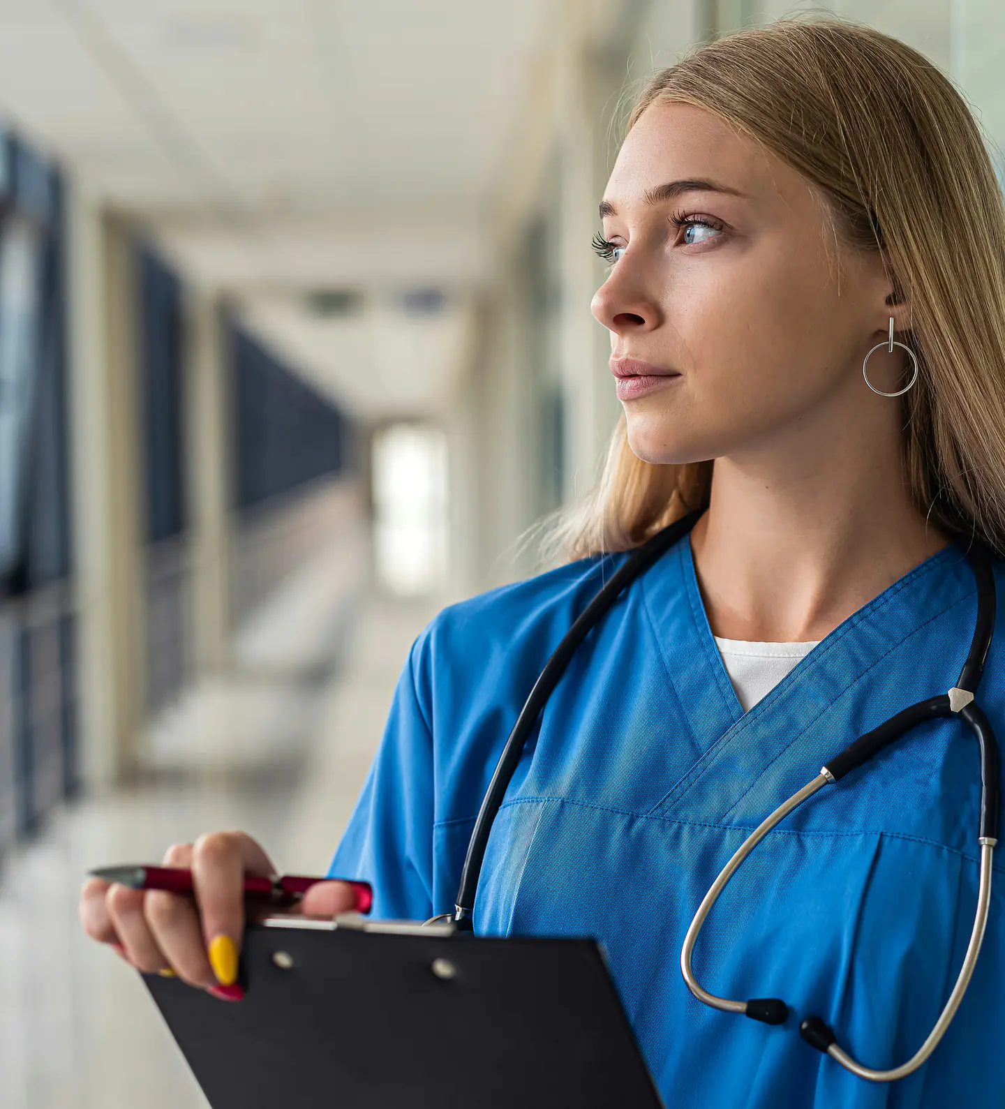 Une infirmière avec un stéthoscope et un porte-documents dans un couloir d’hôpital.