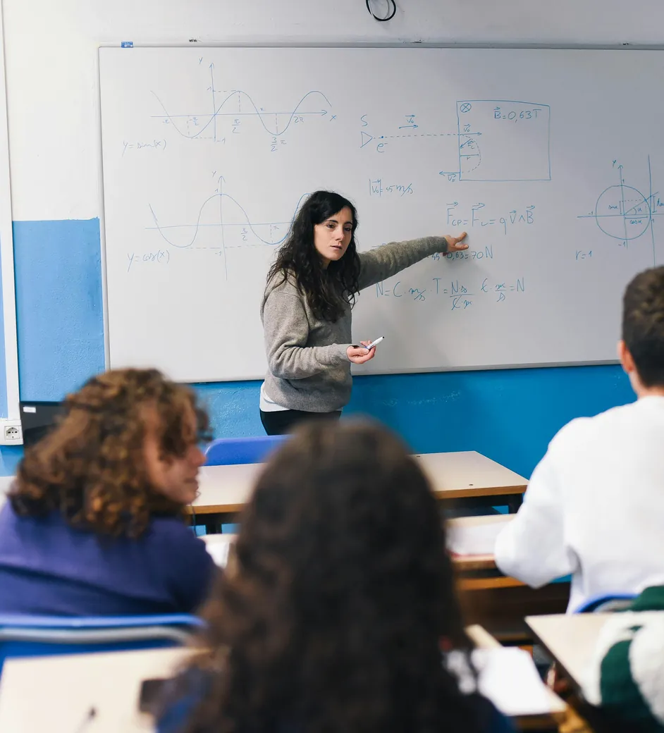 Une enseignante explique un exercice au tableau devant une classe de lycéens vus de dos