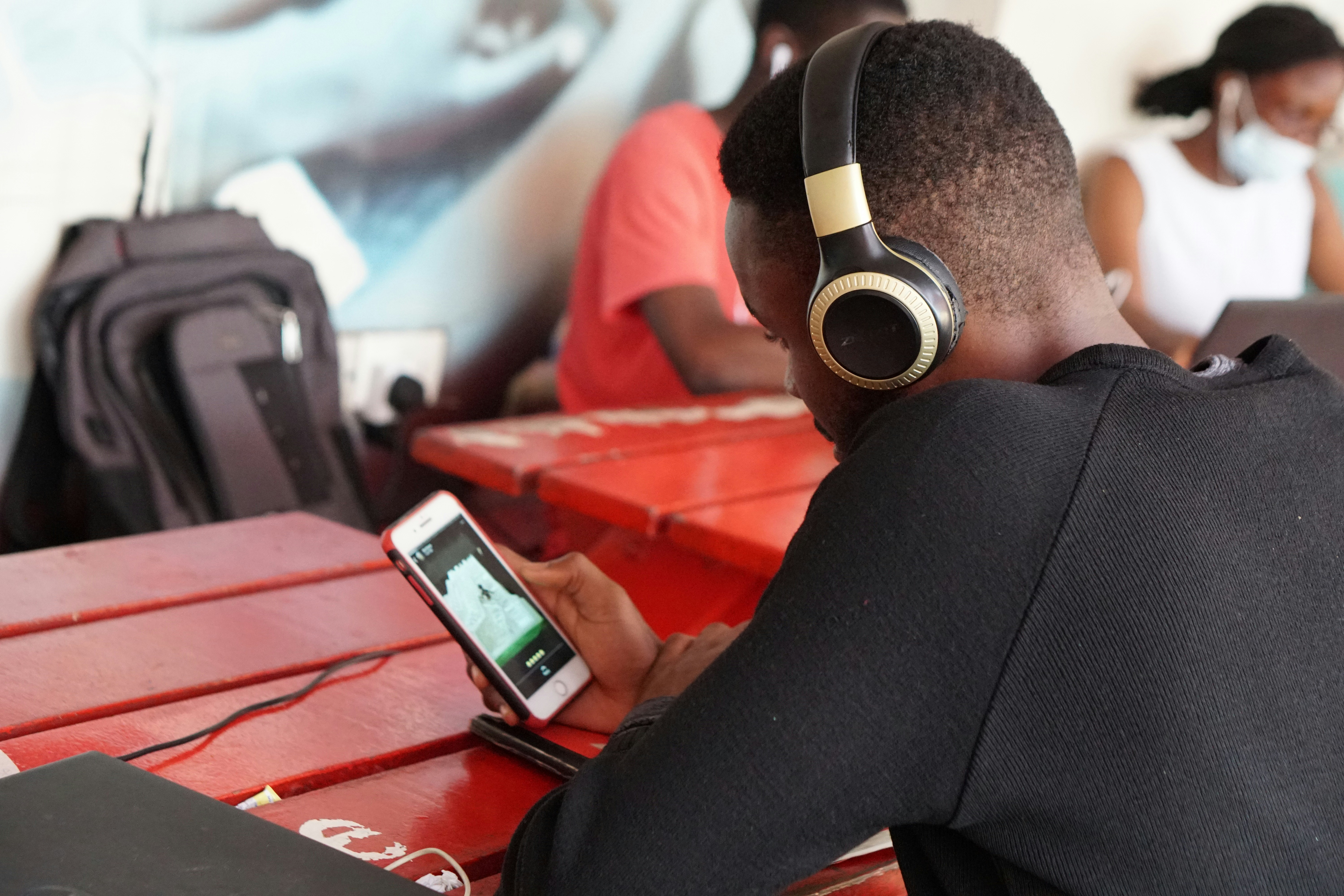 A person working on their phone with headphones on in a public space, representing the portability of mobile music production.
