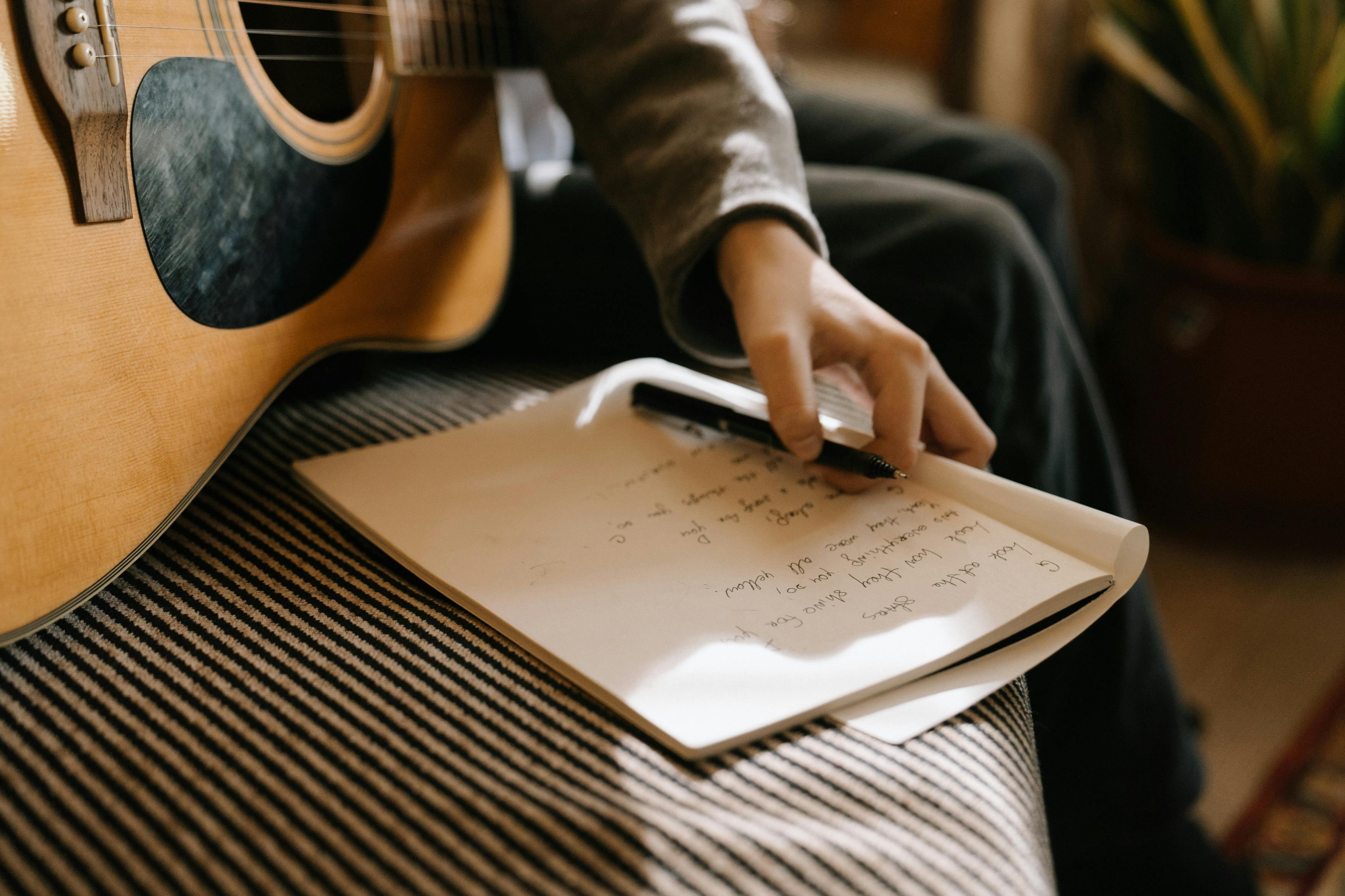 A musician writing lyrics with a guitar on their lap, representing the process of writing country music.