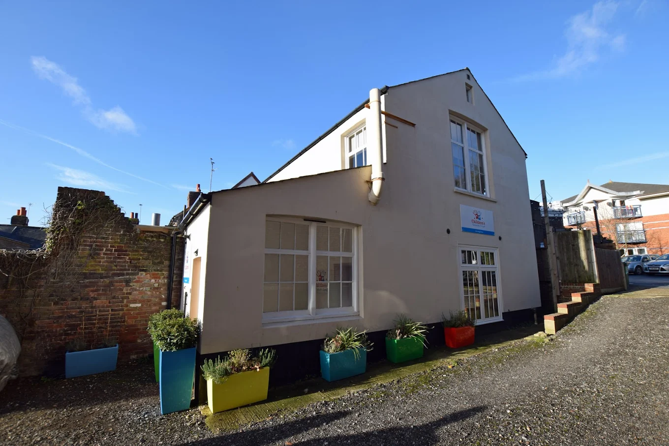 A two-story white building with colorful planters outside, under a clear blue sky.
