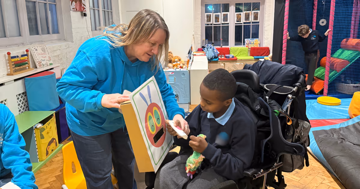 A woman shows a colorful picture to a boy in a wheelchair, who is holding a toy.