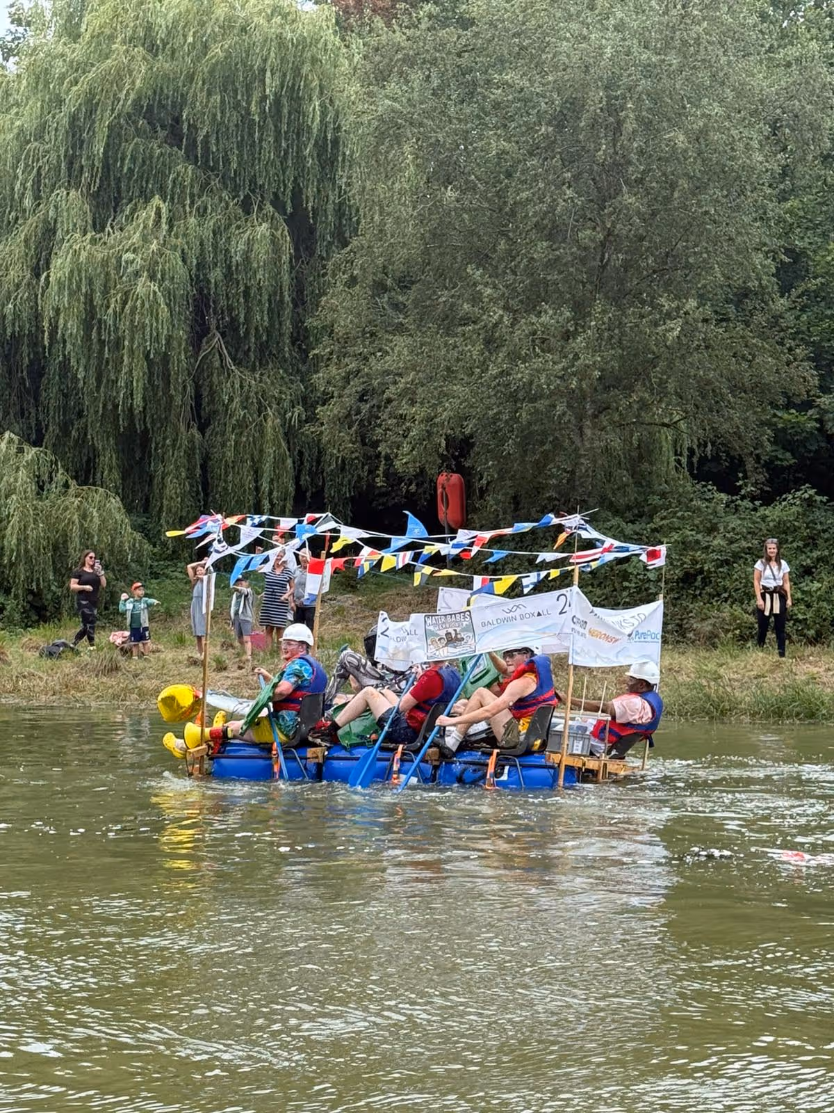 A group of people paddles a homemade raft decorated with flags on a river.