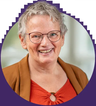 Portret van een glimlachende oudere vrouw met kort grijs haar en een oranje trui.