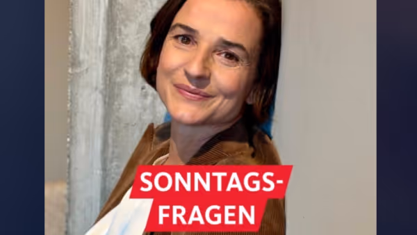 Porträt von Daniela Kielkowski, die leicht lächelnd an eine Betonwand gelehnt ist. Sie trägt eine weiße Bluse und ein braunes Cord-Jacket. In der Ecke steht das WDR 2 Logo, dazu der rote Schriftzug „Sonntagsfragen“.