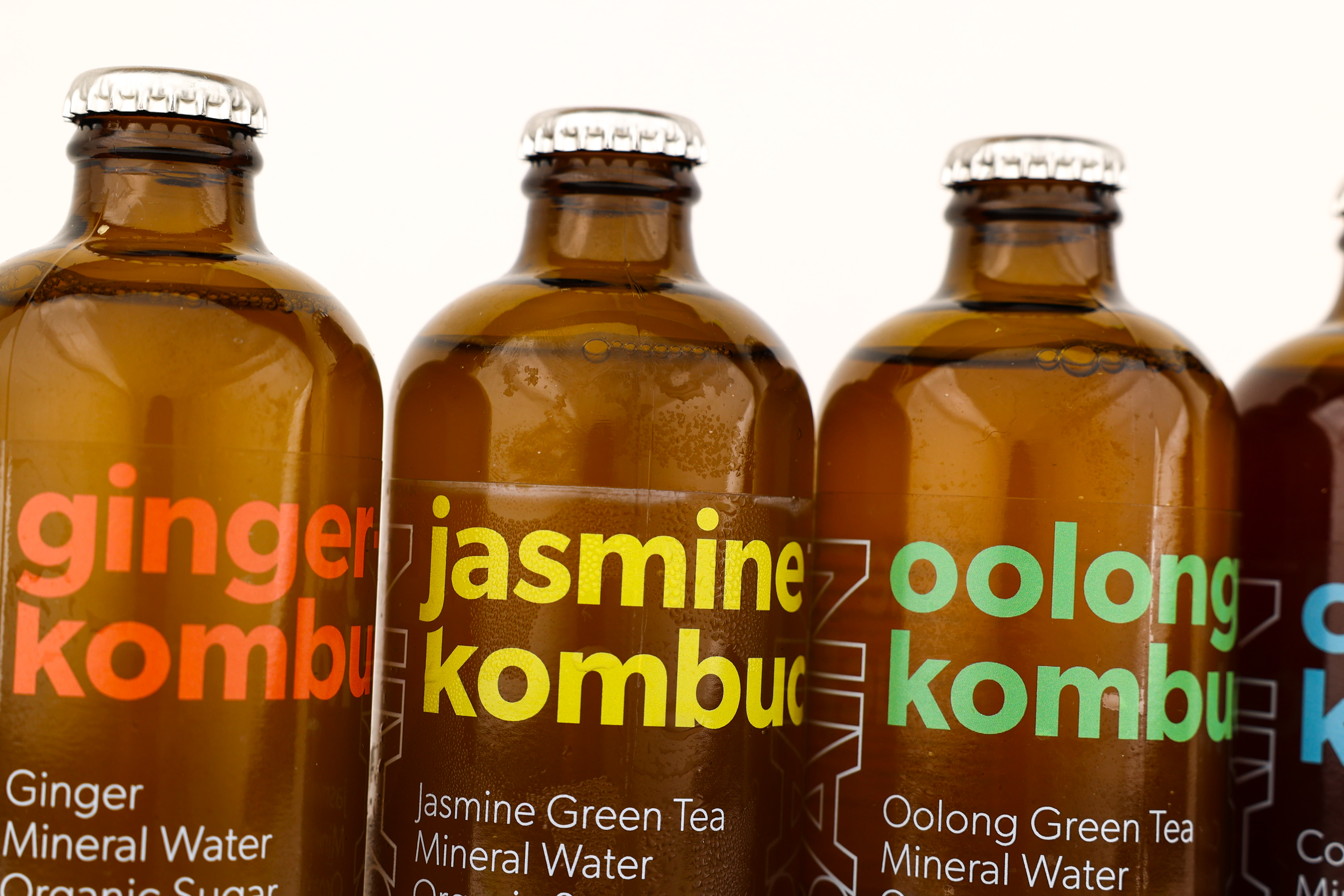Close-up of amber glass bottles with metal caps labeled ginger kombucha, jasmine kombucha, and oolong kombucha.