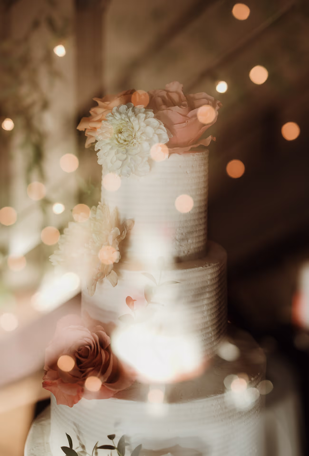 Tiered wedding cake with flowers glowing among string lights at a Roundhouse wedding