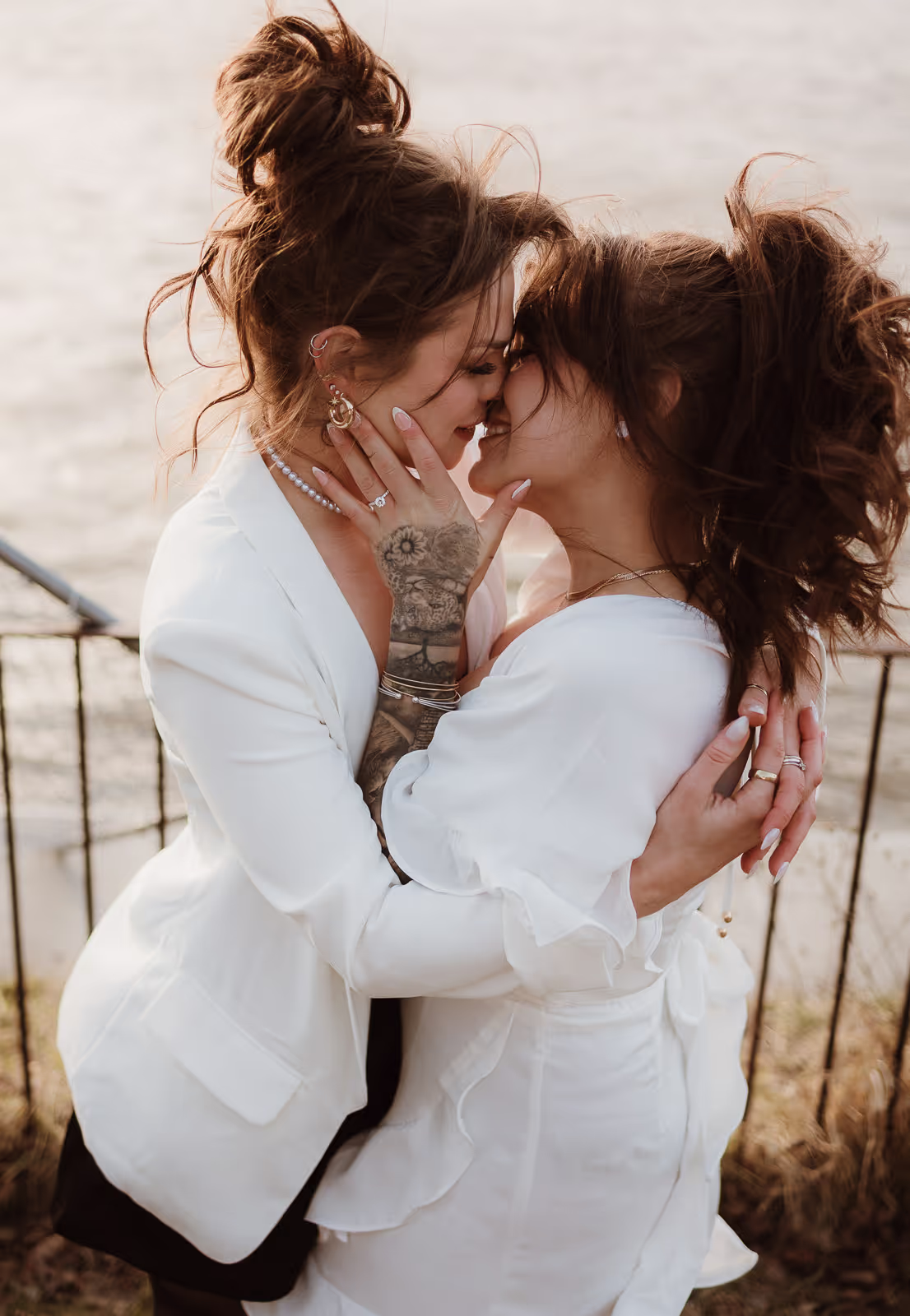 Two women in white embracing and kissing at sunset during a Troy engagement session