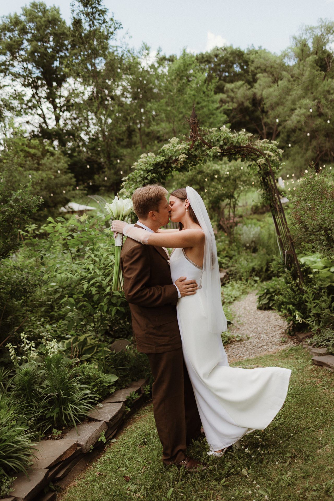 Bride and groom kissing among the greenery at a summer M and D Farm wedding