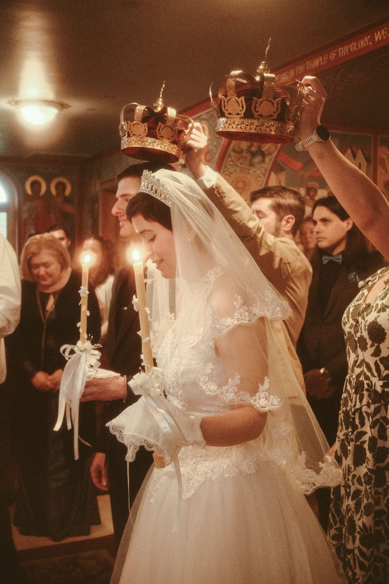 Guests hold ceremonial crowns above a bride and groom by candlelight at a backyard wedding photographed on film