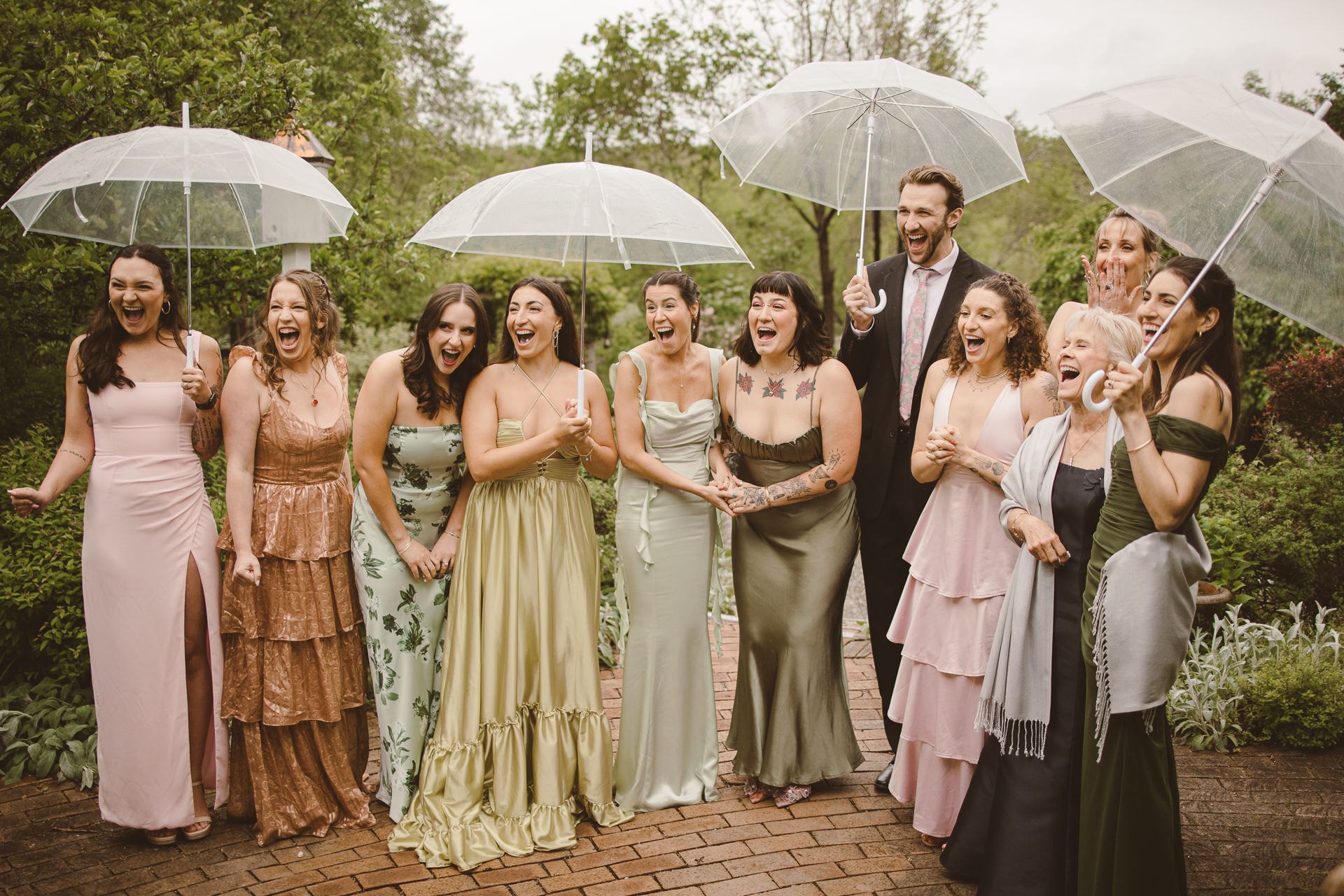 Wedding party laughing under clear umbrellas in the rain at a spring M and D Farm wedding