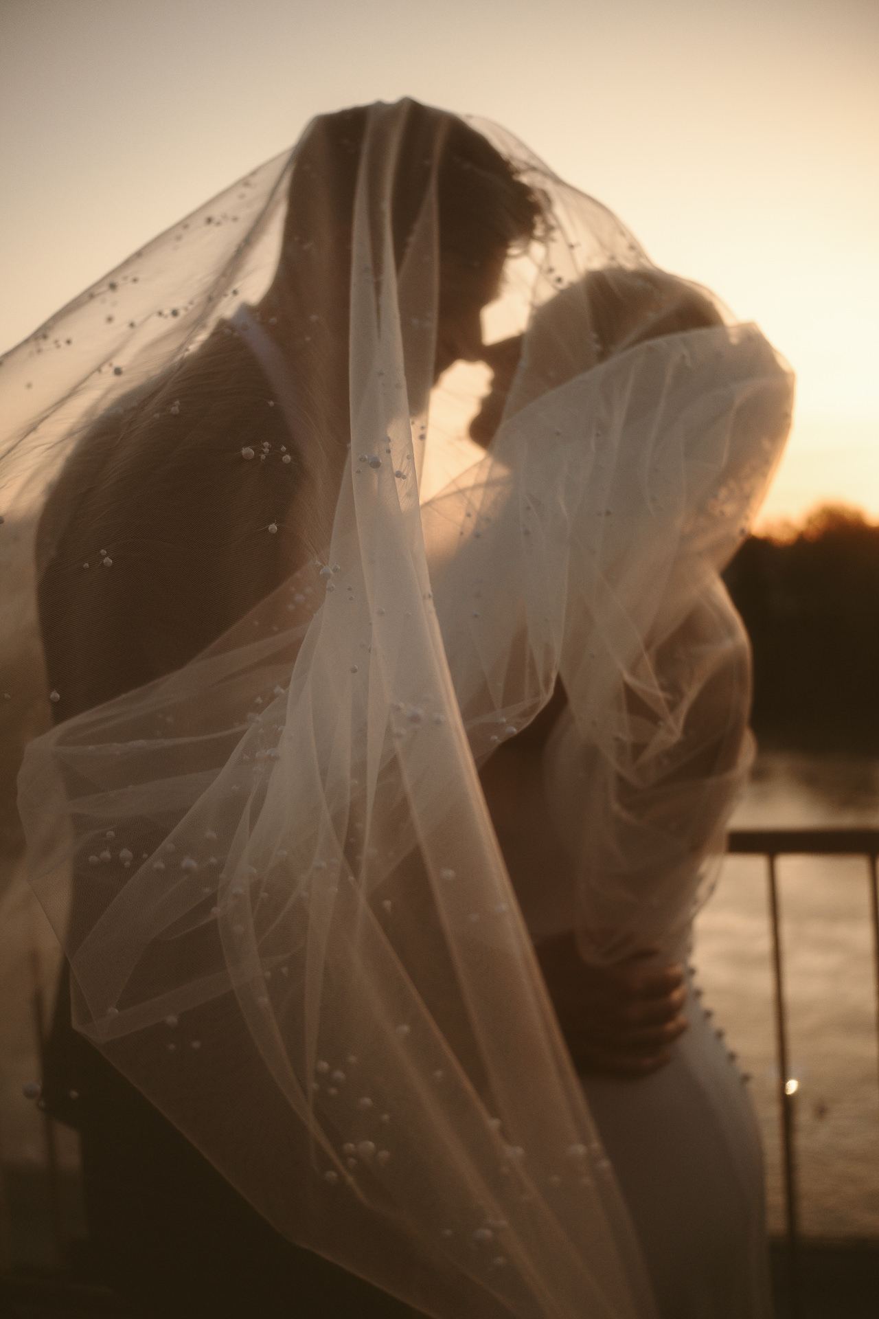 Bride and groom beneath a veil at sunset beside the water at a Revolution Hall wedding