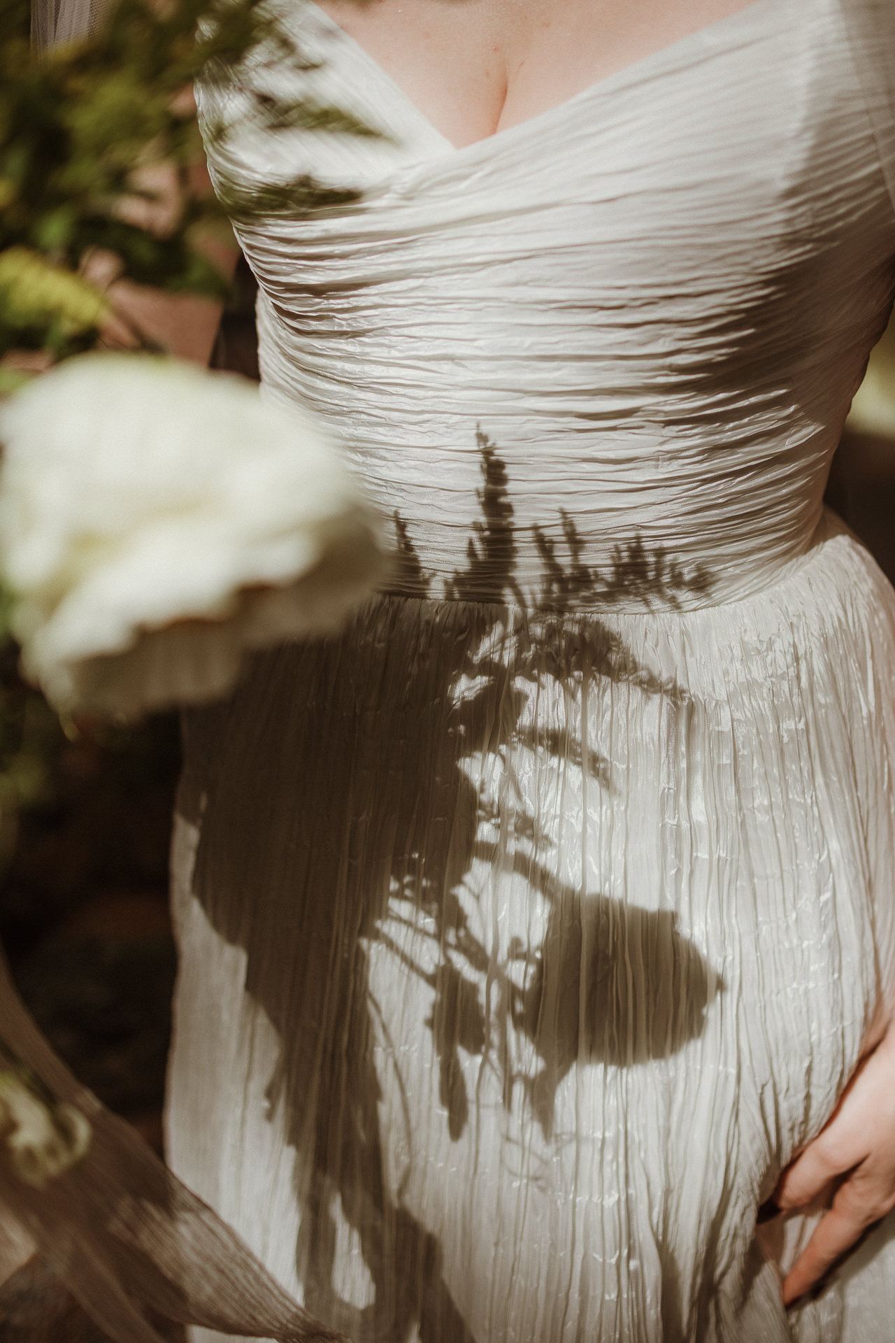 Pleated gown and bouquet in dappled light at a Forest Lake Camp wedding in the Adirondacks