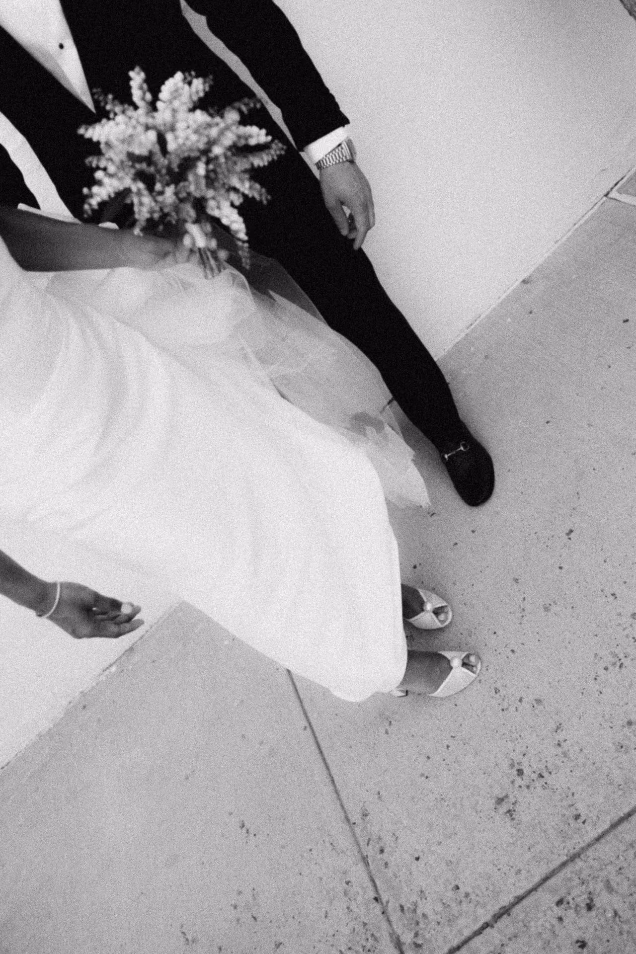 Black and white overhead view of a bride and groom sitting on a stone step with her bouquet