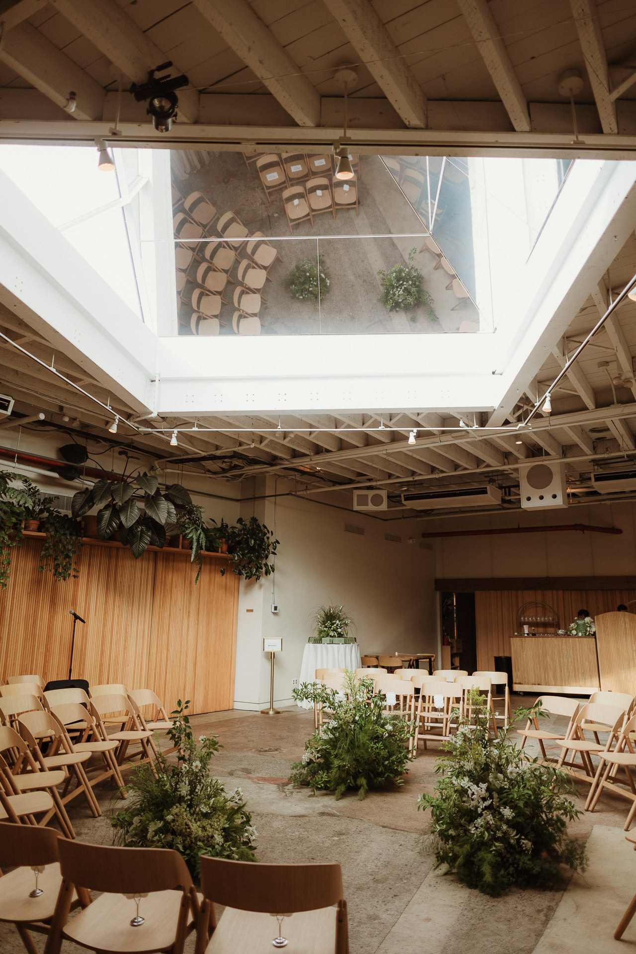 Skylit ceremony space with wooden chairs and potted greenery at a Rule of Thirds wedding