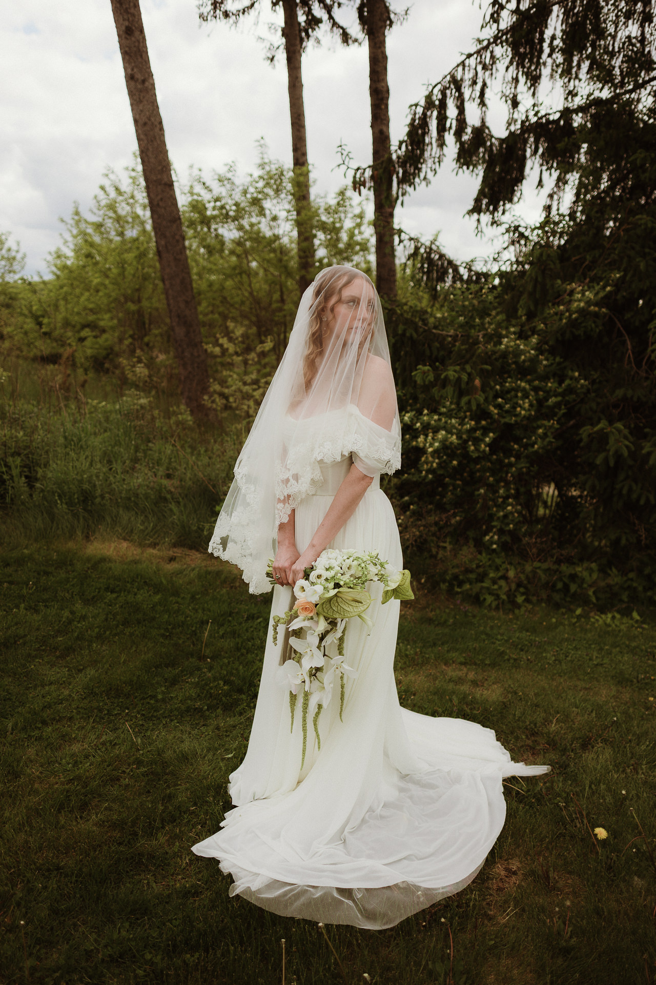 Veiled bride holding calla lilies in a green meadow at a spring Garrison wedding