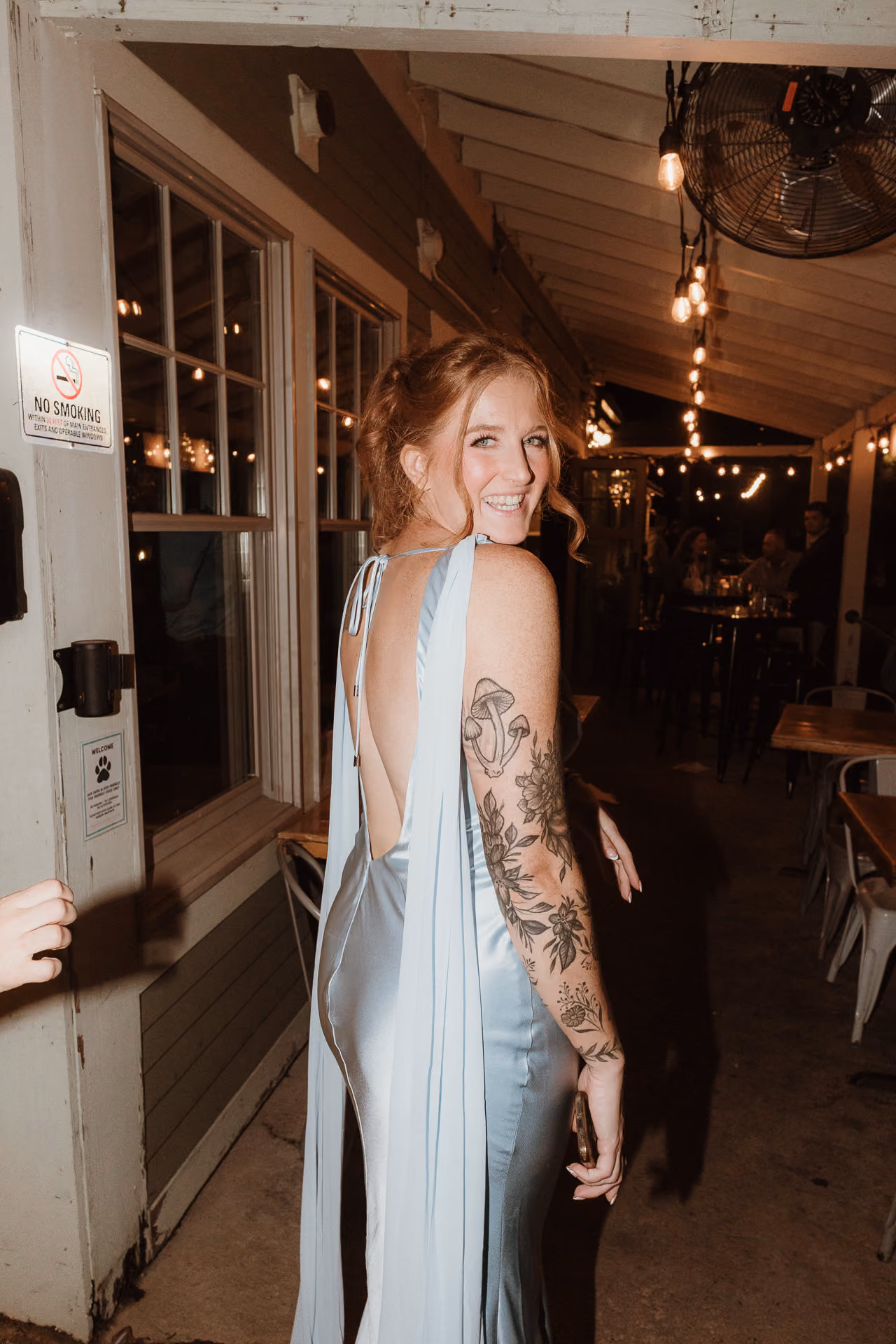 Smiling bride in a pale blue satin gown in a string-lit doorway at a welcome party