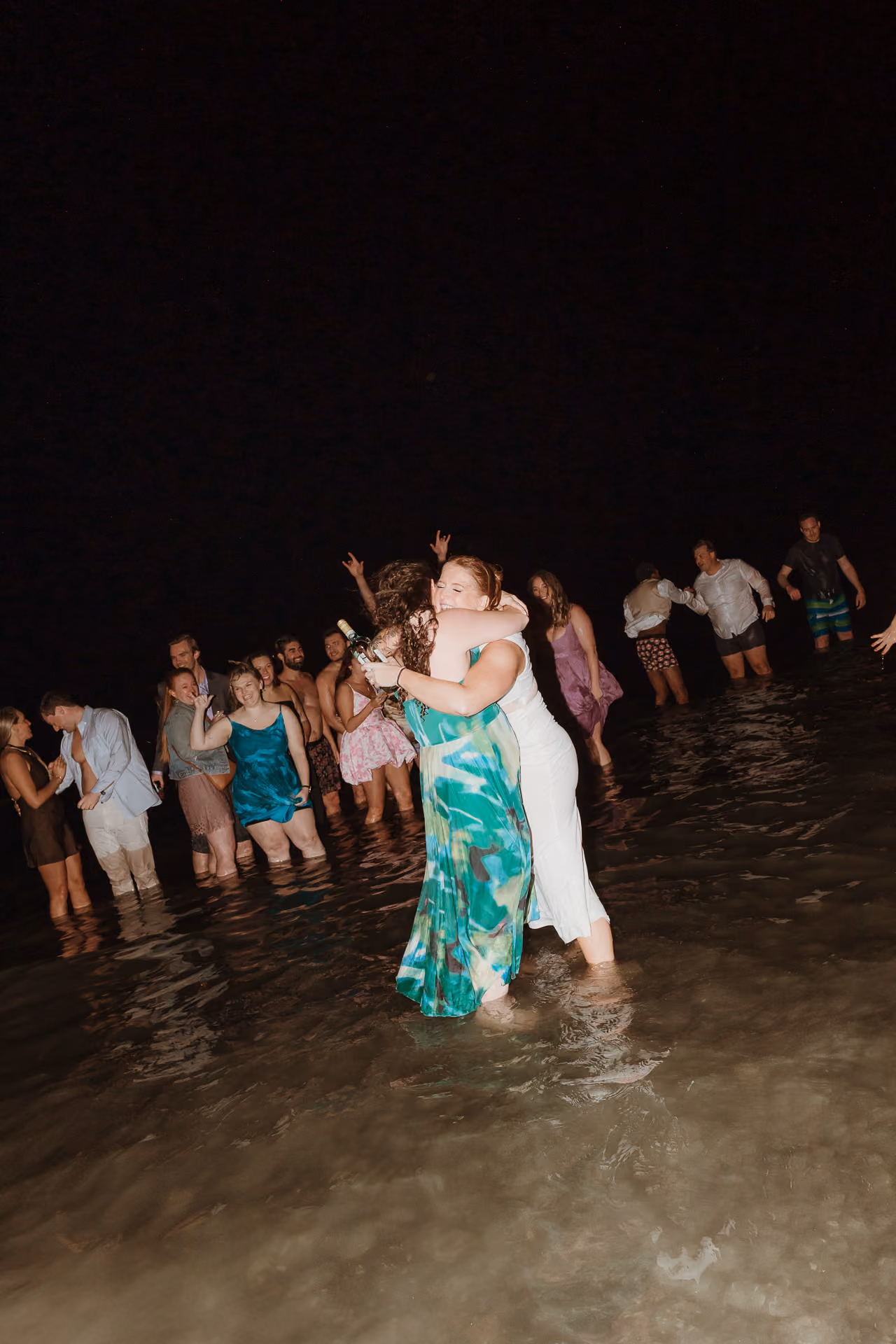 Guests wading and dancing in the water at night at a welcome party