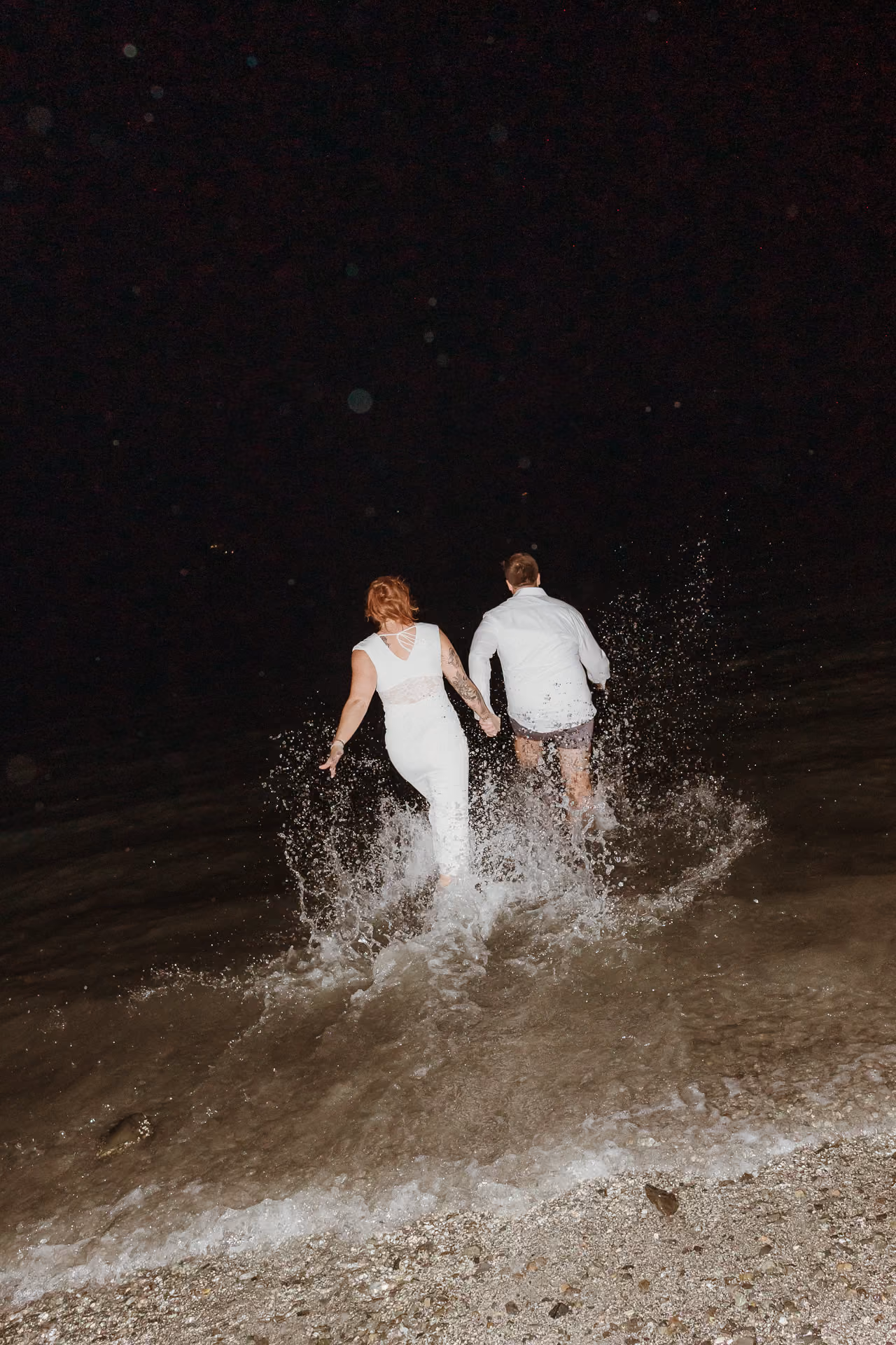 Couple running hand in hand into the lake at night at a welcome party