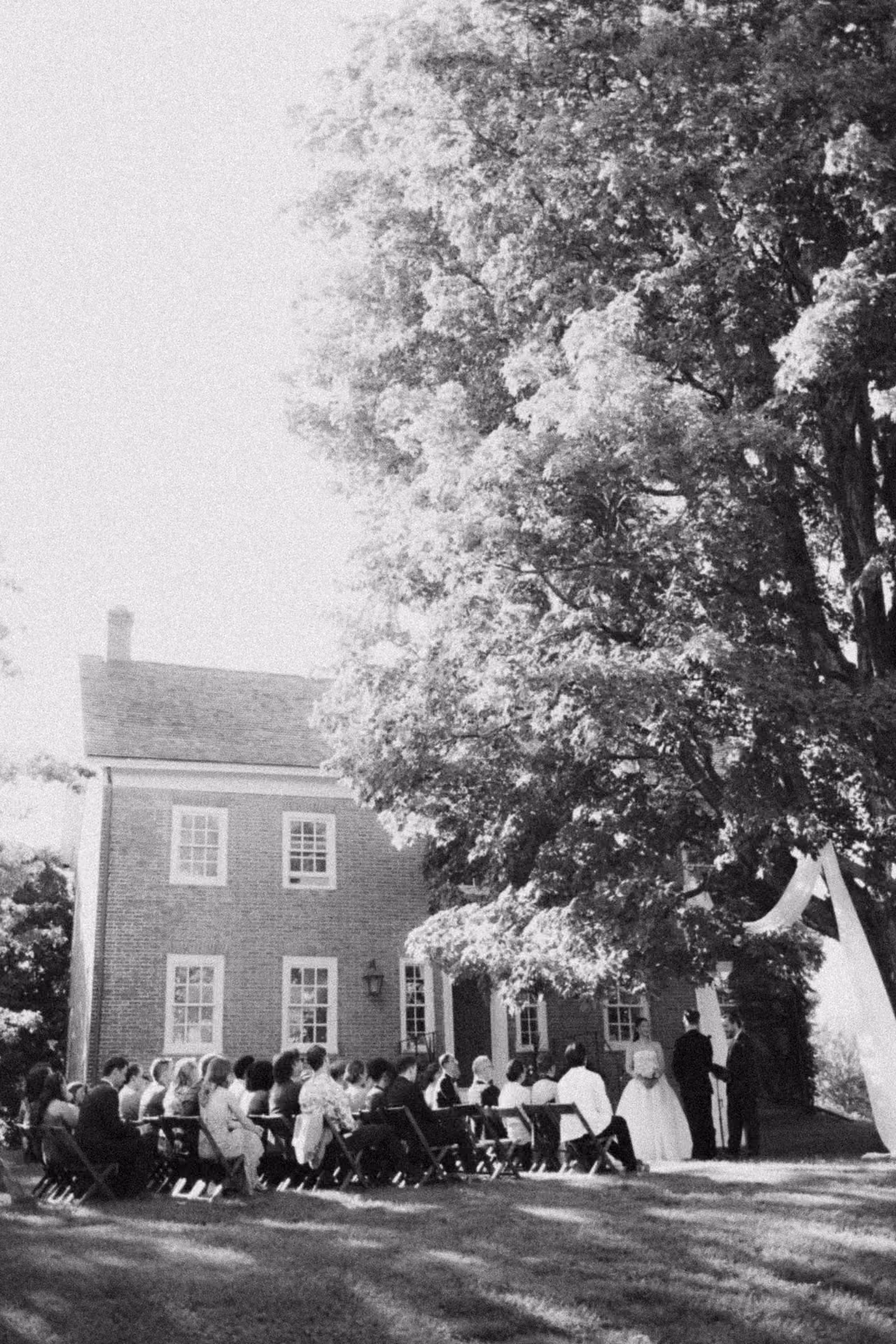 Black and white photograph of an outdoor ceremony beside a brick house at Windrift Hall