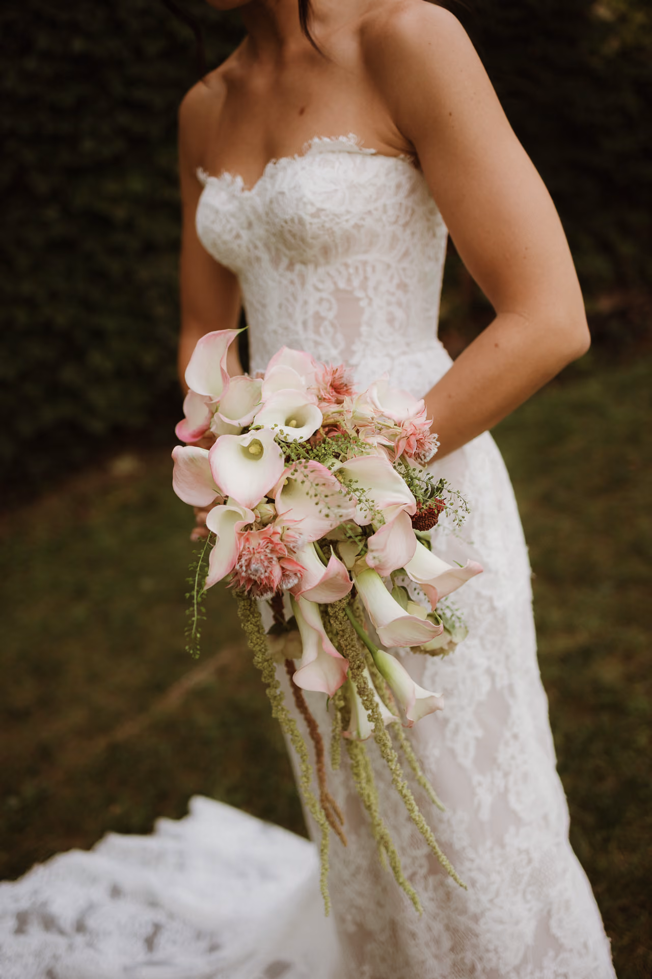 Bride in a lace strapless gown holding a cascading calla lily bouquet at Windrift Hall