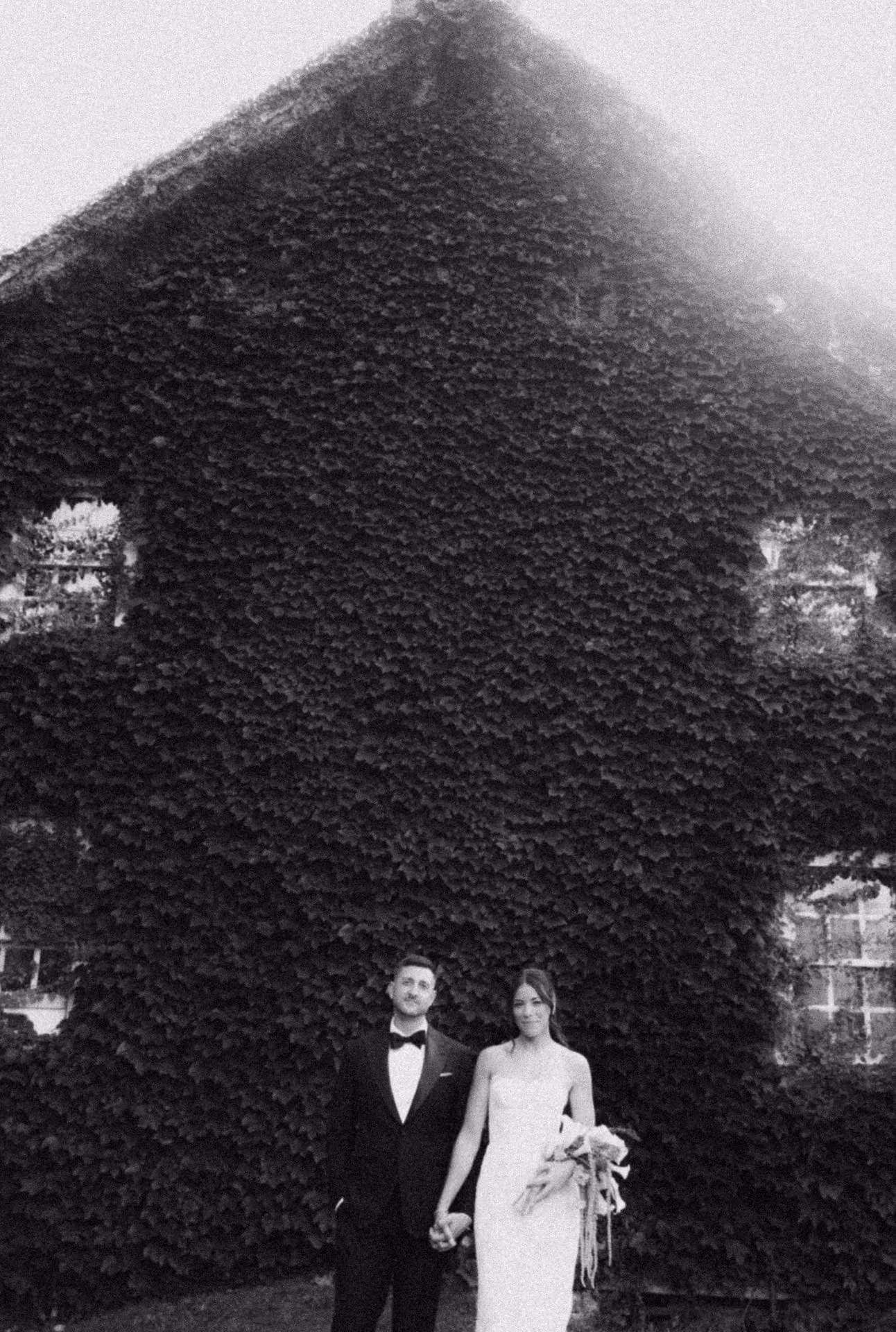 Black and white photograph of a bride and groom in front of an ivy-covered wall at Windrift Hall