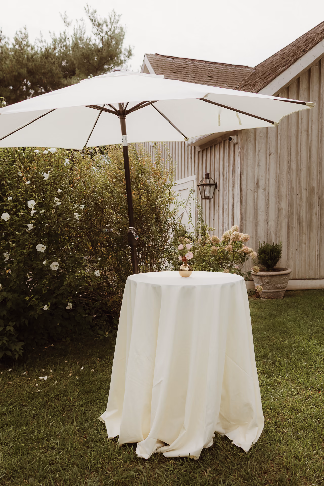 Cocktail table under a white umbrella beside a cedar-shingled building at Windrift Hall