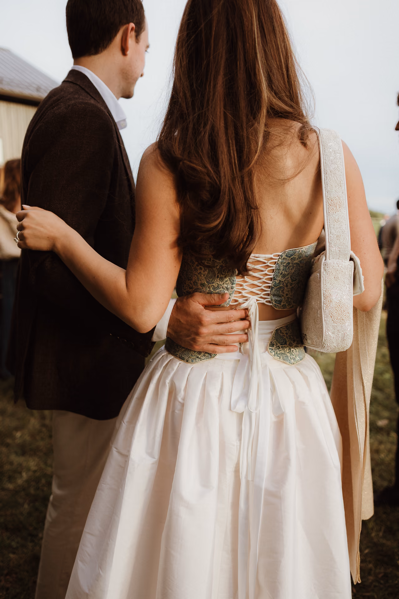 Couple embracing from behind, her lace-up corset back visible, at a Camptown welcome party