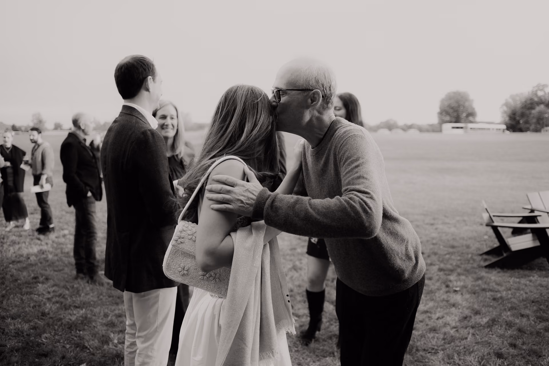 Black and white photograph of guests greeting with a kiss on a lawn at a Camptown welcome party