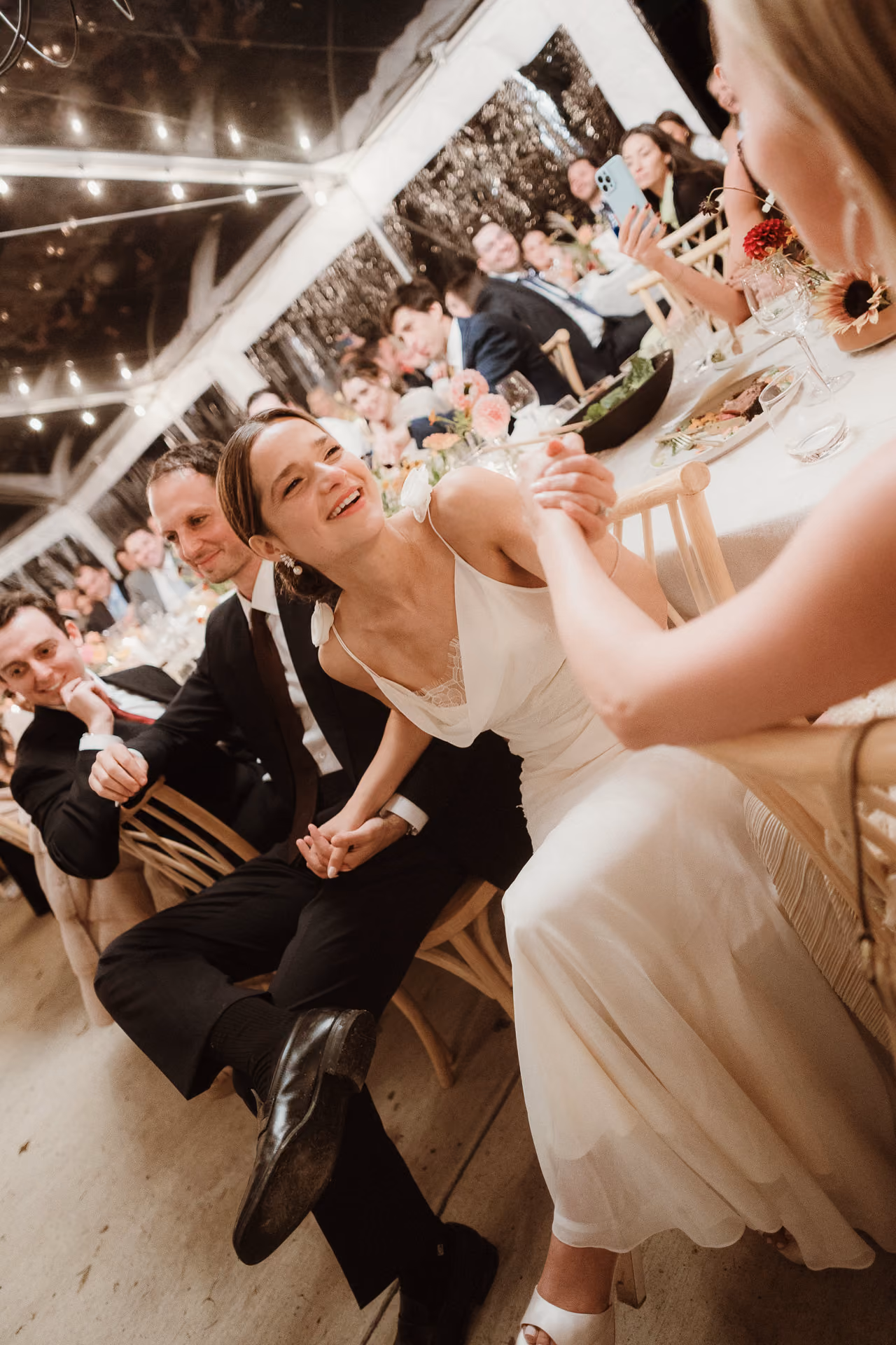 Bride laughing with guests at a long string-lit table at a Camptown wedding