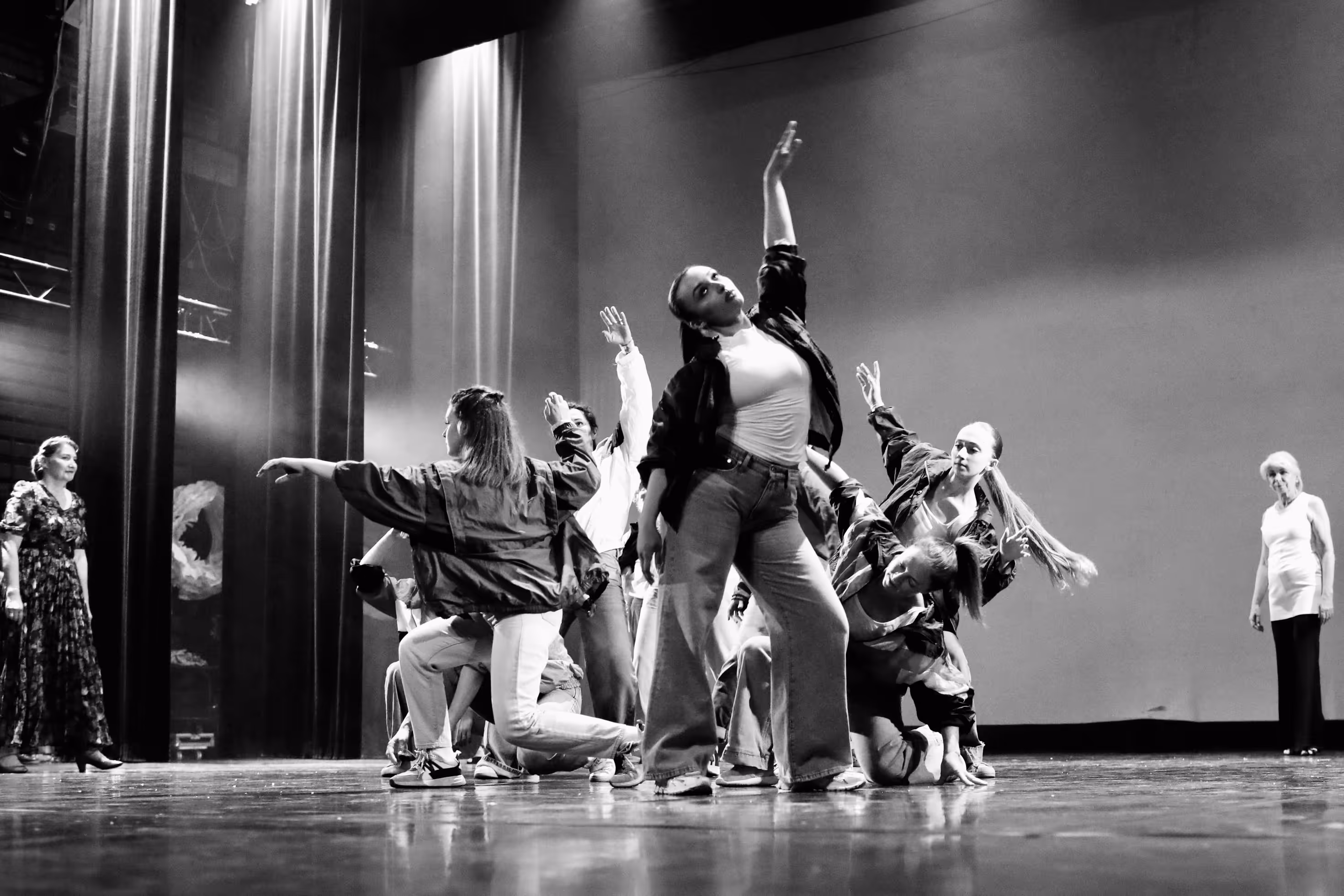 Groupe de danseurs en poses dynamiques sur scène avec deux spectateurs féminins sur les côtés.