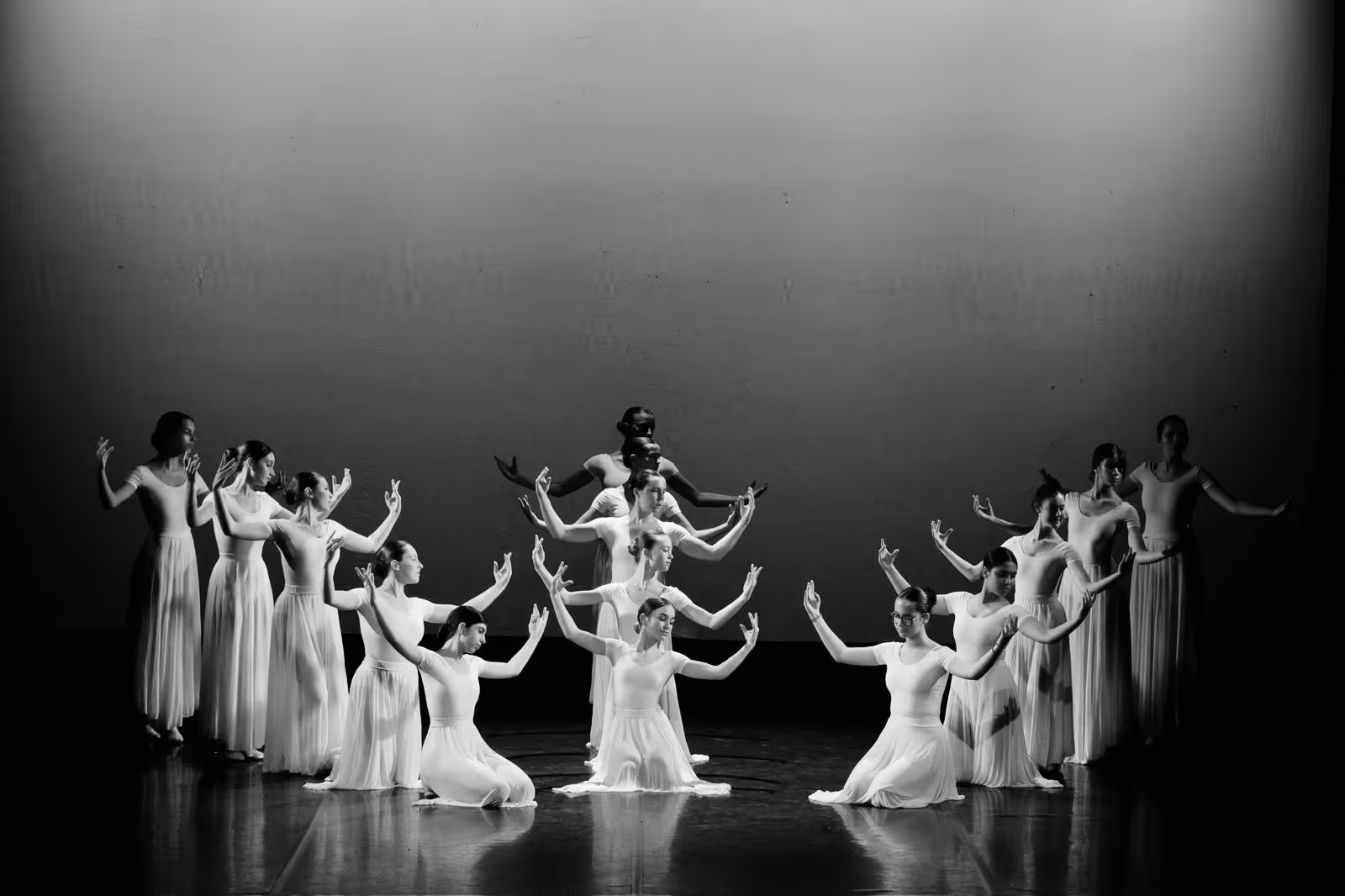 Groupe de danseurs en robes longues blanches effectuant une chorégraphie synchronisée sur scène.