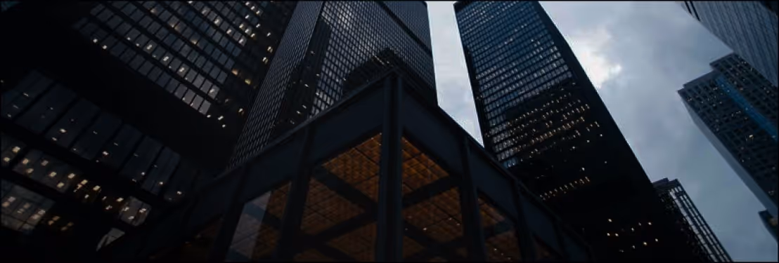 Low-angle view of tall office buildings with glass windows against a cloudy sky at dusk.