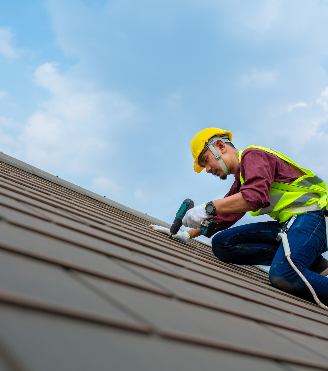 Roofer in florescent green reflective gear hand drilling in slate roofing system 