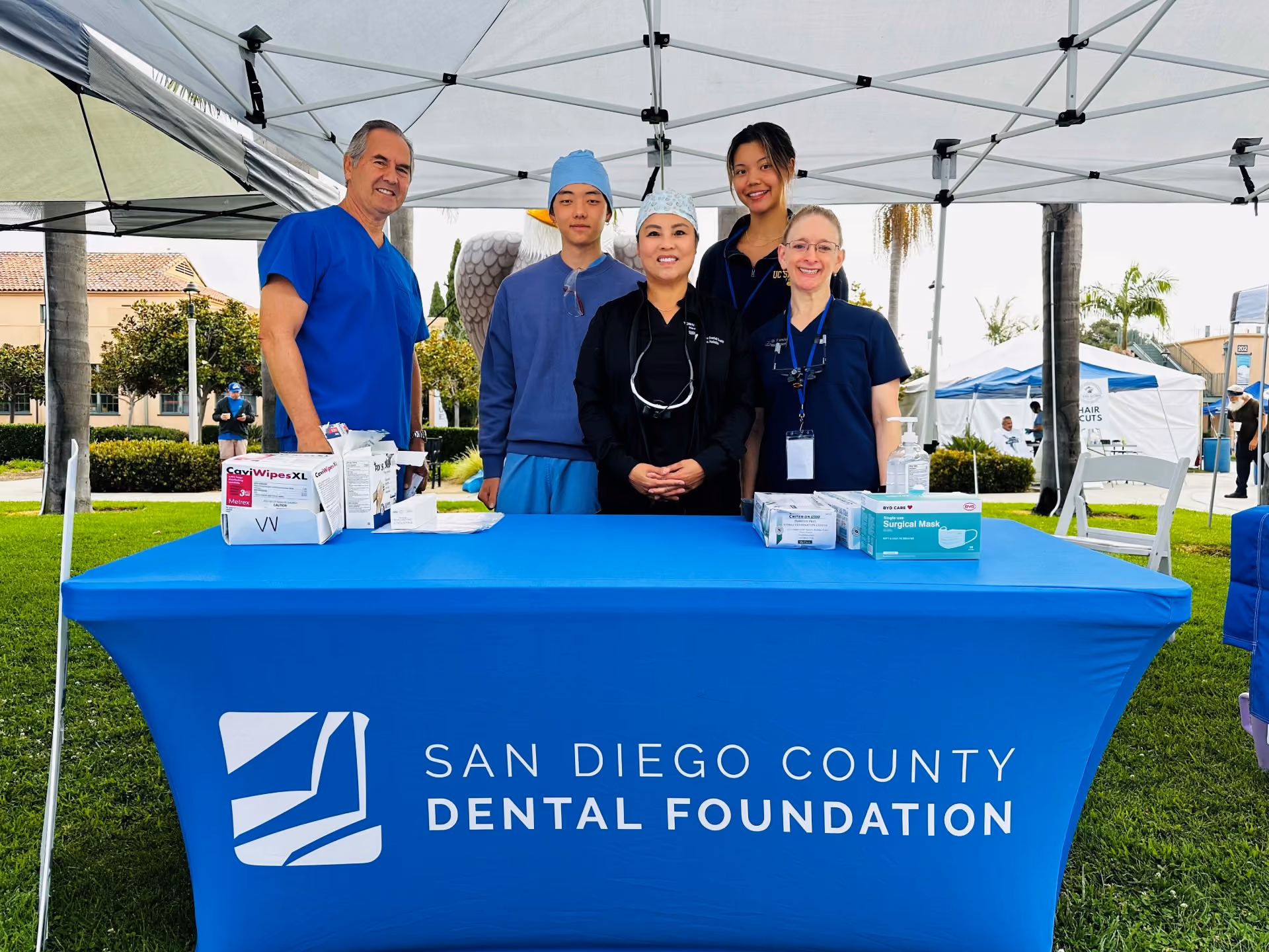 Five dental professionals standing behind a San Diego County Dental Foundation table under a canopy outdoors.