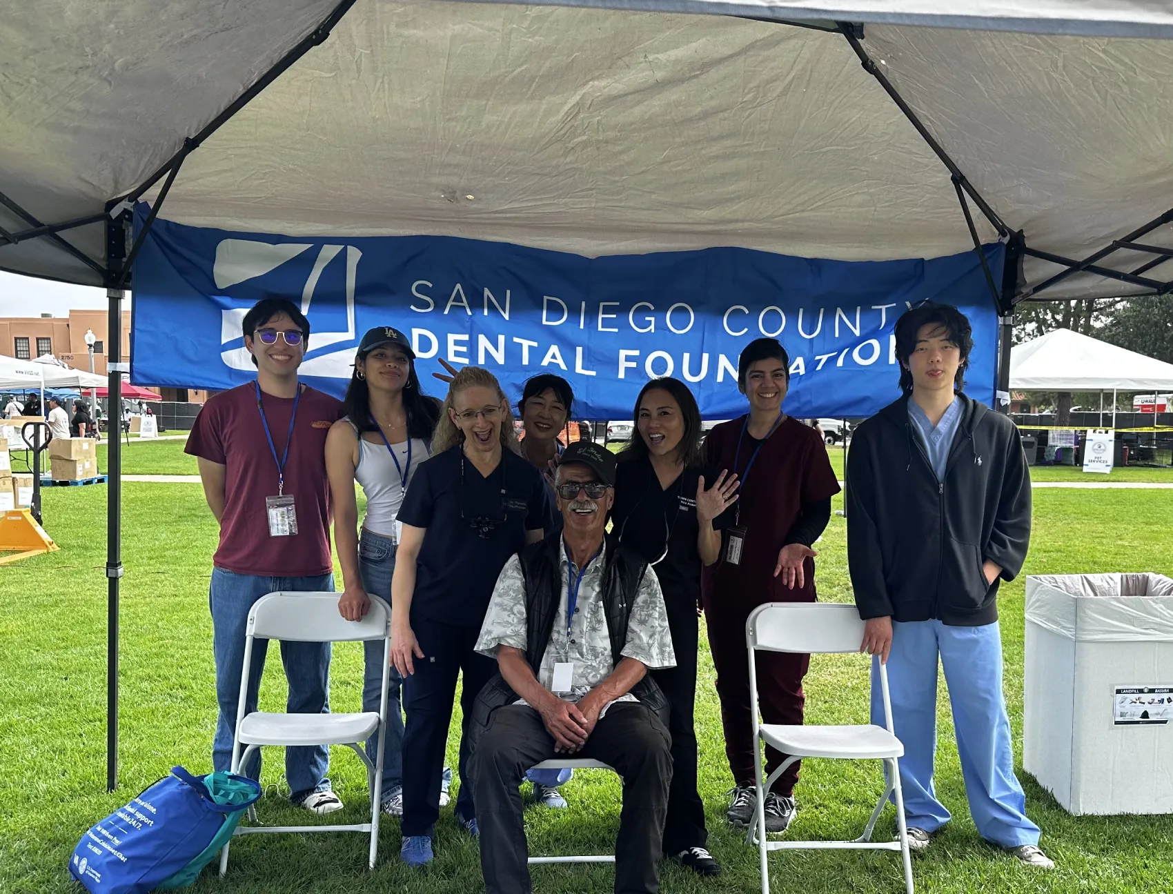 Group of eight people smiling under a tent with San Diego County Dental Foundation banner behind them.