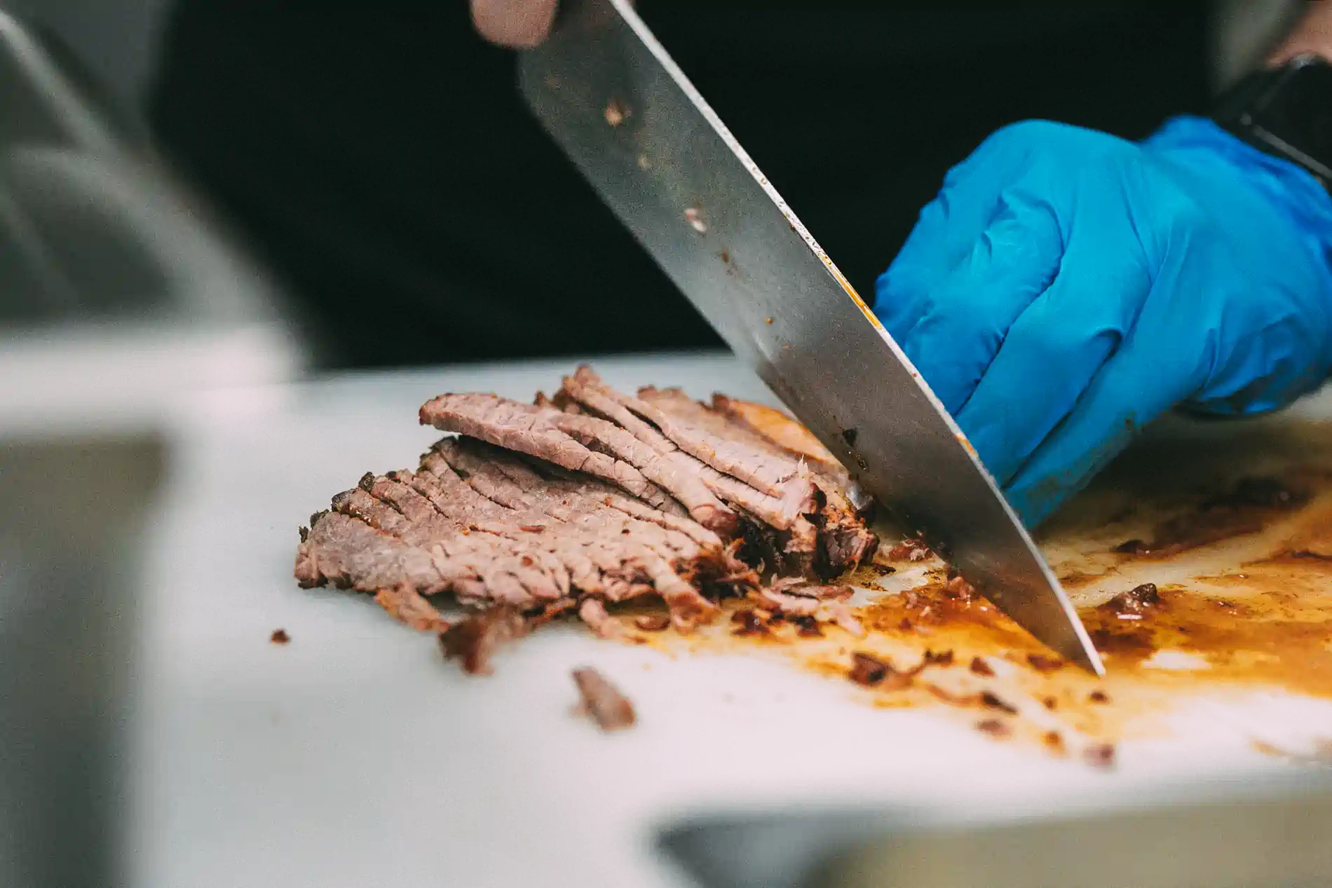 A person wearing blue gloves slices cooked meat on a cutting board.