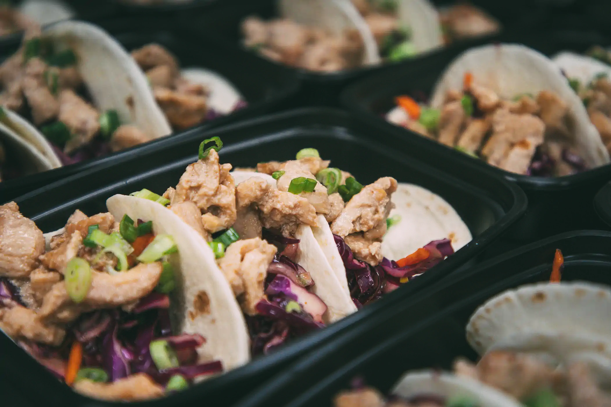 Close-up of meal prep containers filled with chicken tacos, garnished with green onions and served with a colorful slaw. The tacos are part of the Fed by Jed meal prep and delivery service in Milwaukee.