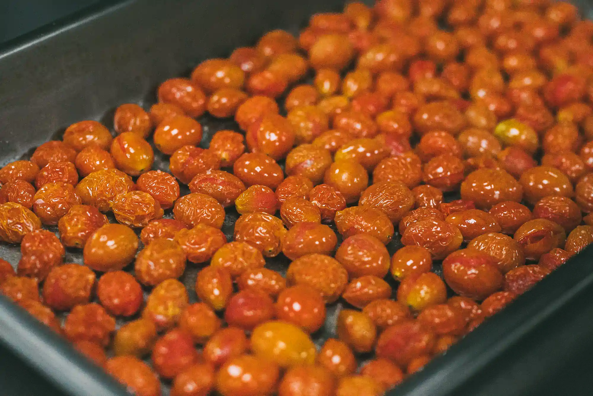 A tray of roasted cherry tomatoes with a slightly wrinkled texture.