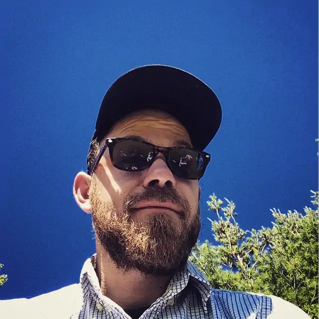 portrait of graphic designer jesse maule, a man outside in sunglasses with a dark beard with trees and sky in the background