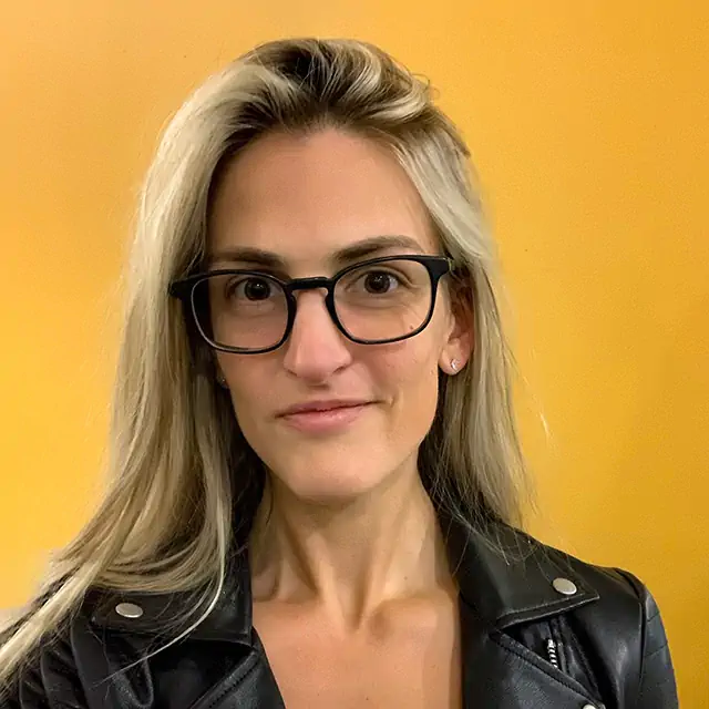 portrait of photographer heather mrotek, a woman with blond hair in a leather jacket against a yellow background