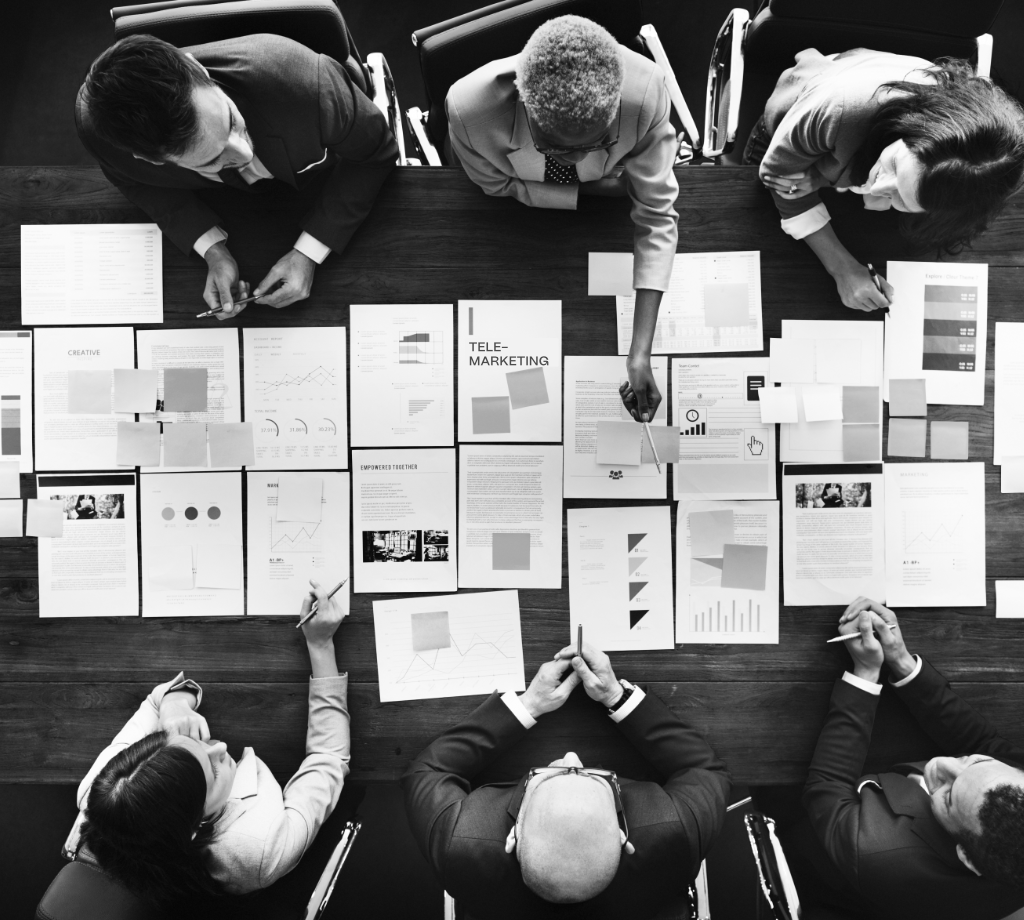 Ein Meeting aus der Vogelperspektive, die Teilnehmer sitzen auf zwei gegenüberliegenden Seiten eines Tischesg