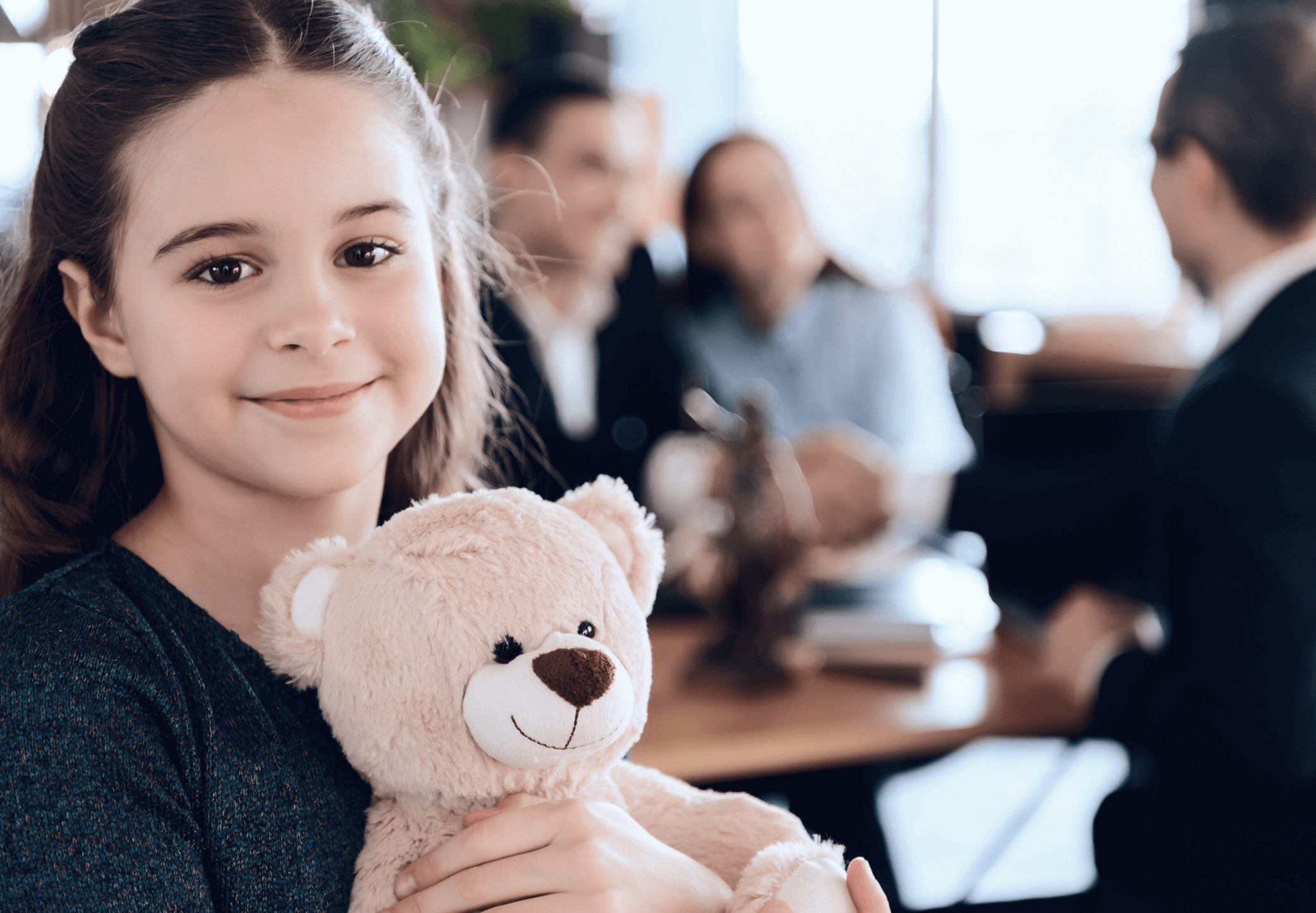 Girl holding a teddy while parents are talking with a laywer or attorney