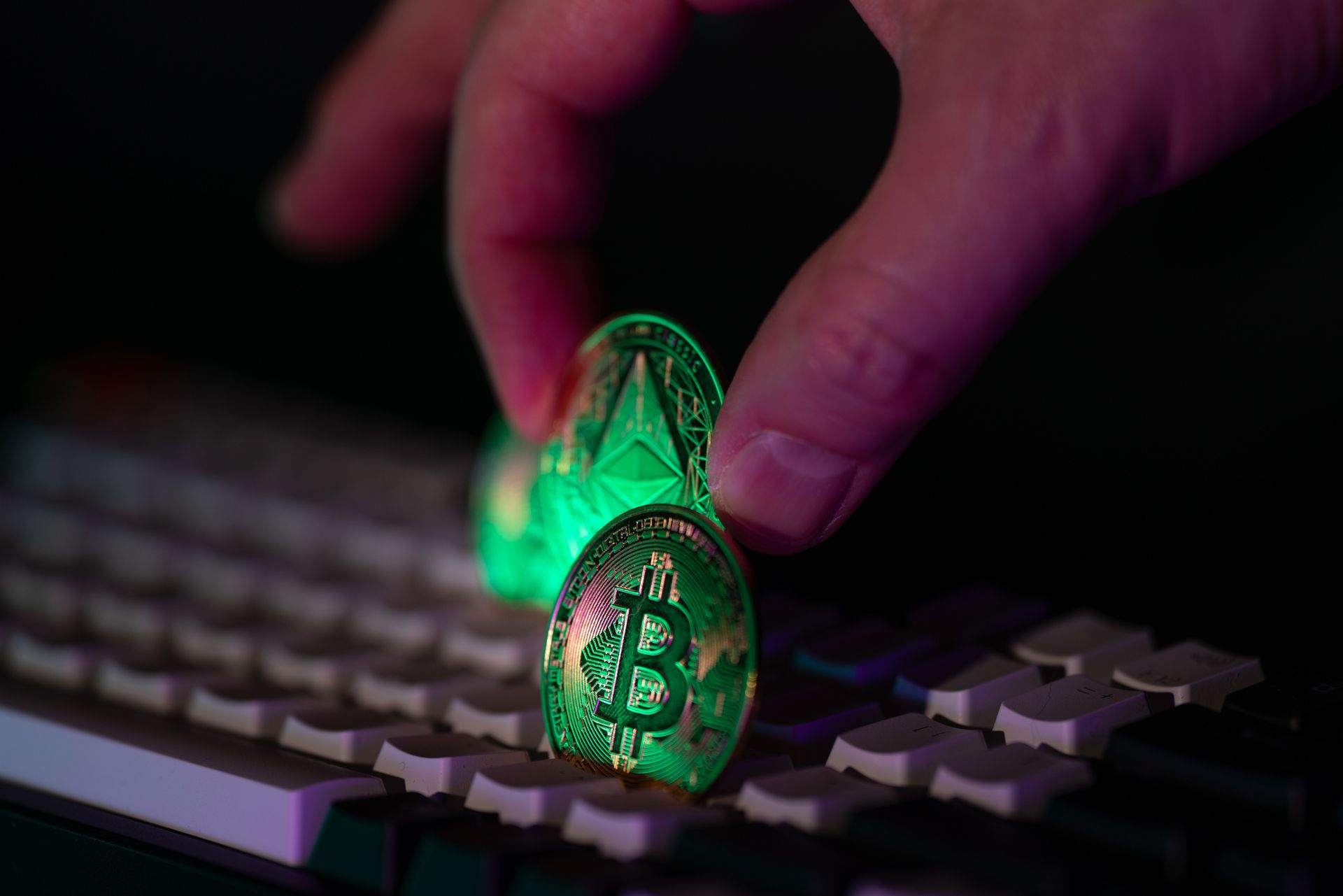 Hand placing a Bitcoin coin and Ethereum coin on a reflective surface, representing cryptocurrency fraud and money laundering