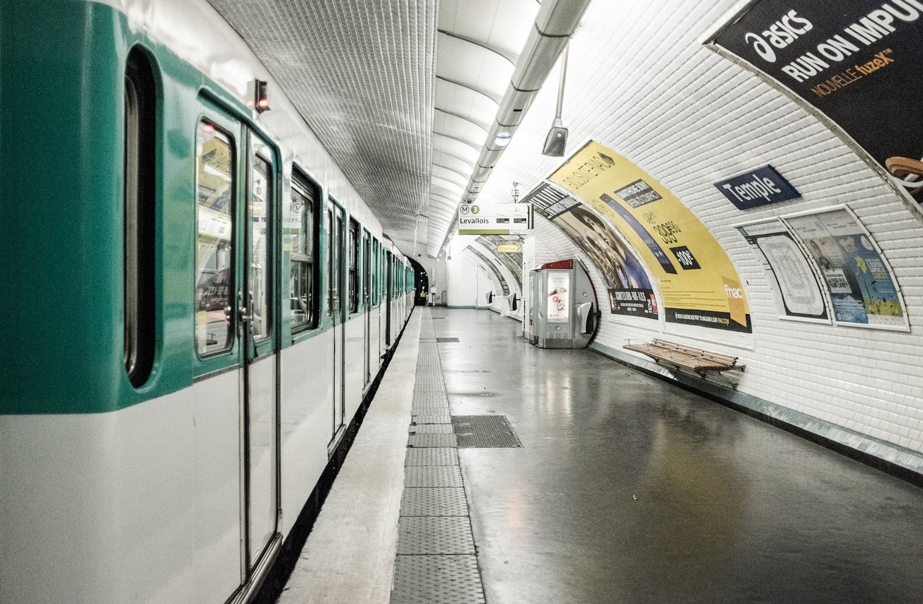 Empty Paris Metro station platform with subway train and advertising posters.