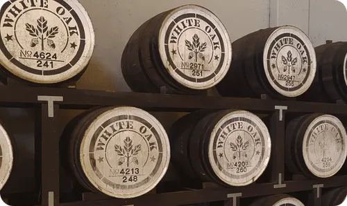 Rows of wooden barrels labeled 'White Oak' stacked on dark wooden racks in a storage area.